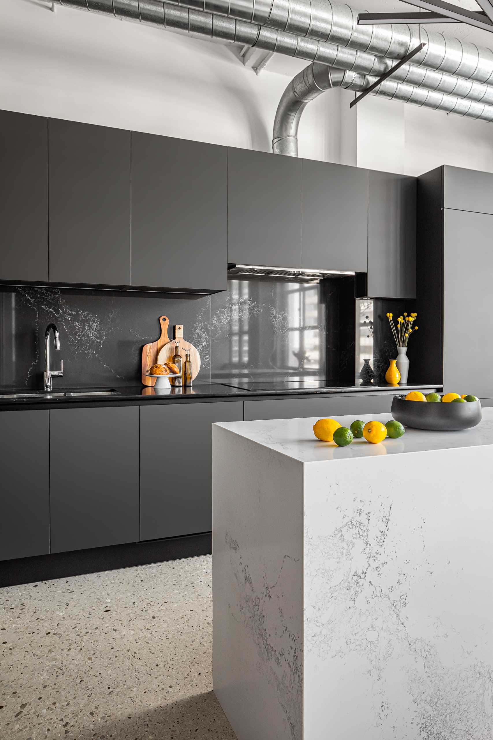 A modern kitchen with a white stone island with subtle veins and minimalist hardware-free black cabinets.