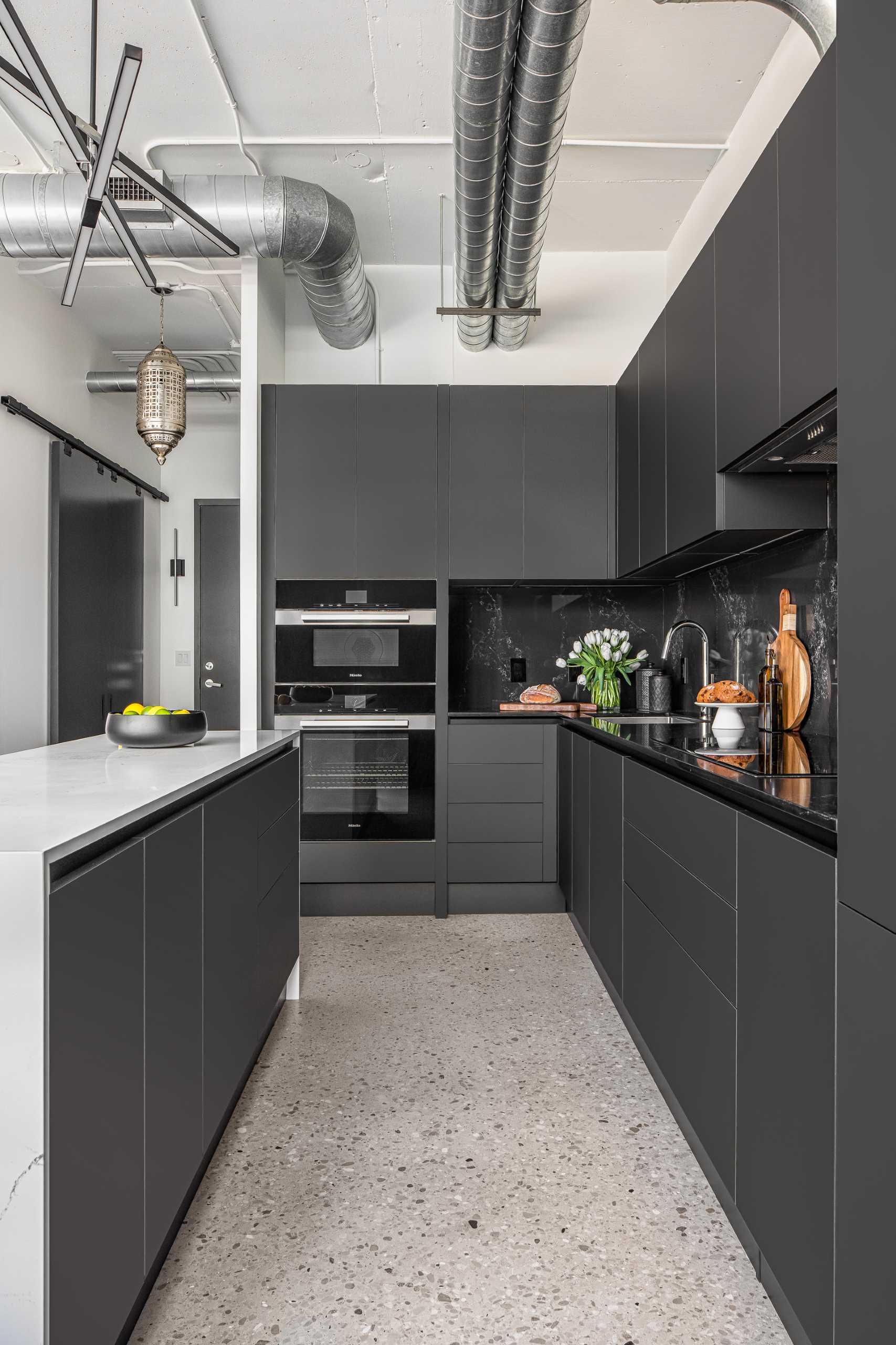 A modern kitchen with a white stone island with subtle veins and minimalist hardware-free black cabinets.