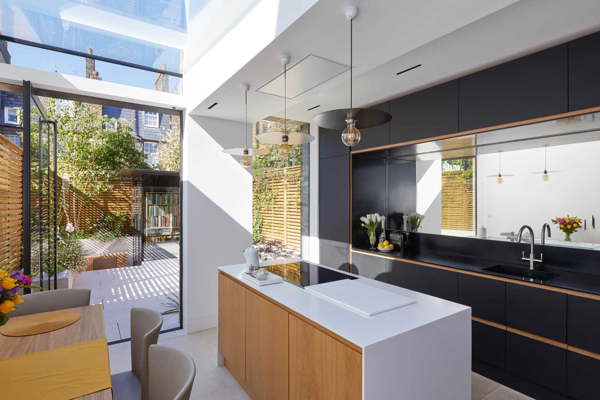 This modern rear addition includes a new kitchen with an island and a small dining area. A partial glass ceiling as well as a floor-to-ceiling window in the kitchen provide ample natural light.