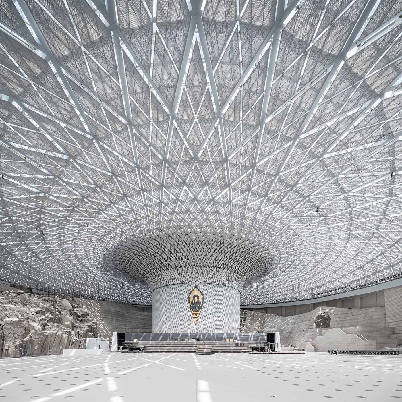 Located on the site of an abandoned quarry, the Maitreya Dharma Hall has a single-shelled glass roof covering the colossal space, while a vertical structural element is inserted in the center for vertical ventilation, equipment, and structural reasons, connecting the ground and the roof space