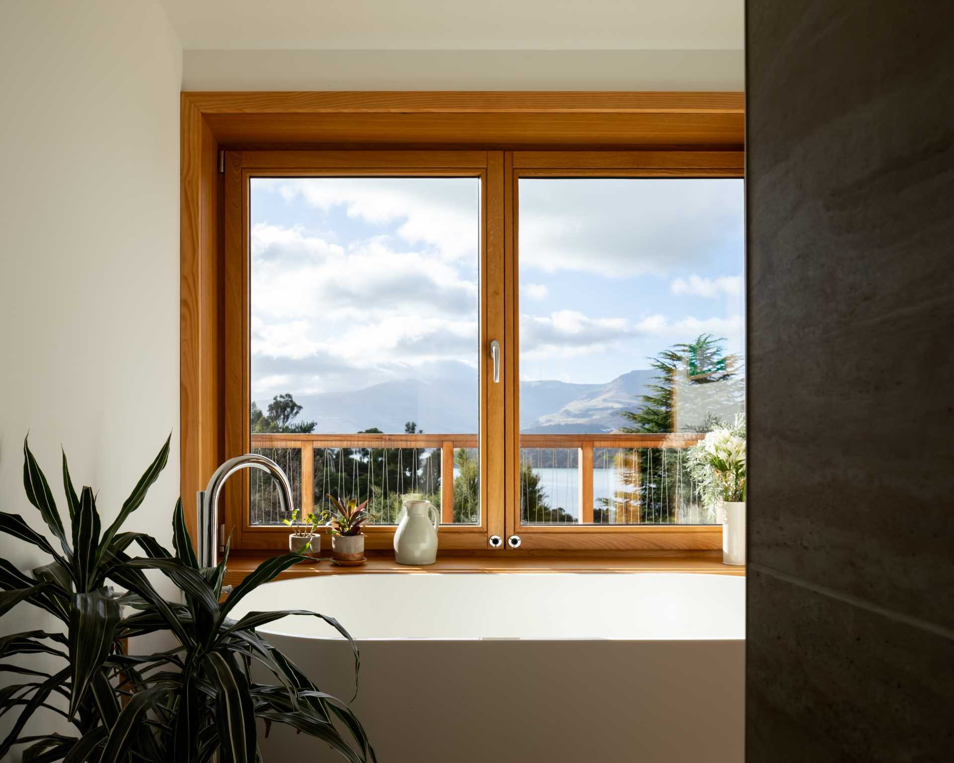 This modern bathroom has a white bathtub positioned under the windows to take advantage of the views.