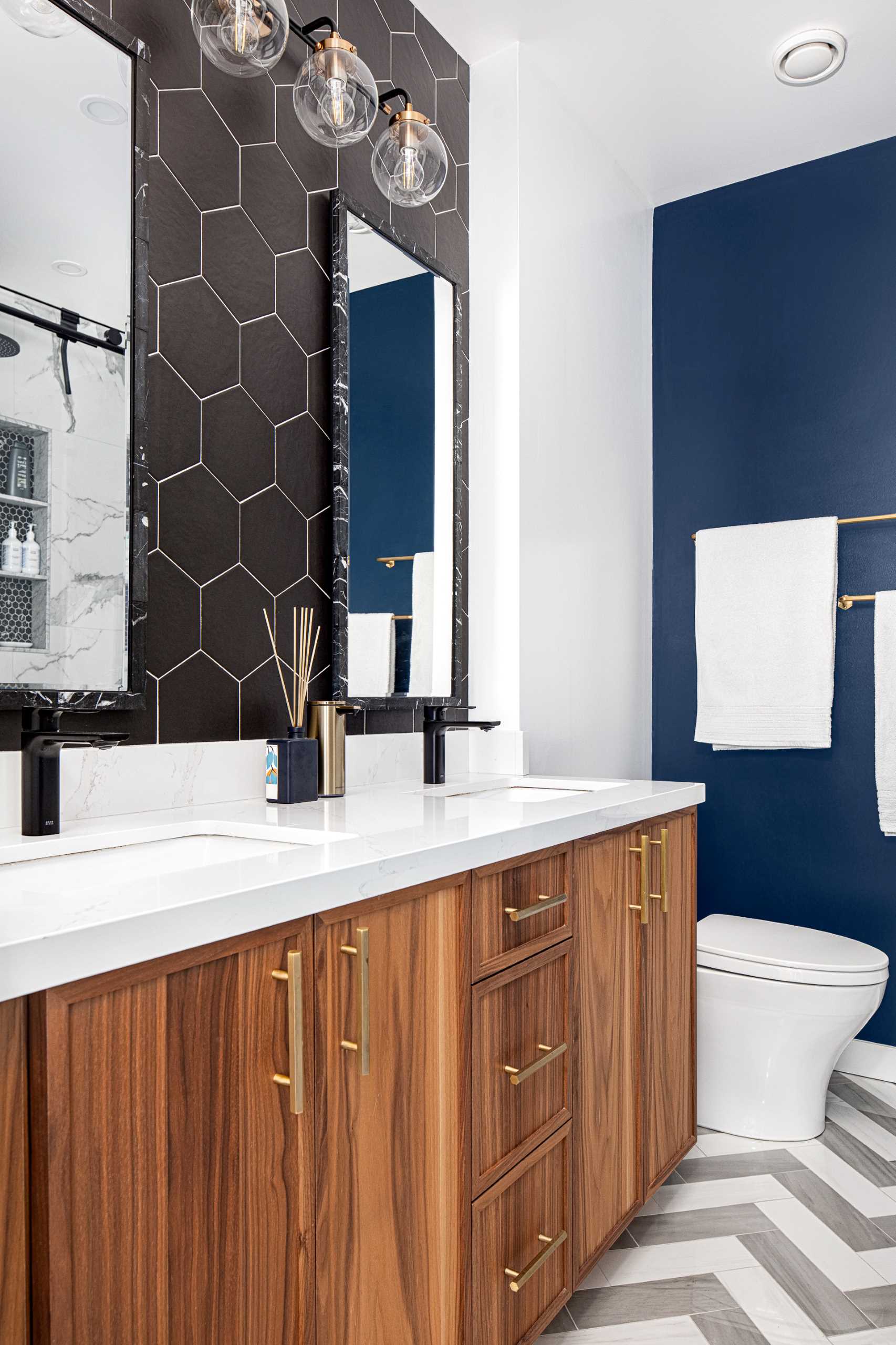 In this bathroom, black hexagonal tiles with white grout line the wall, while another wall, painted a deep blue adds a touch of color.