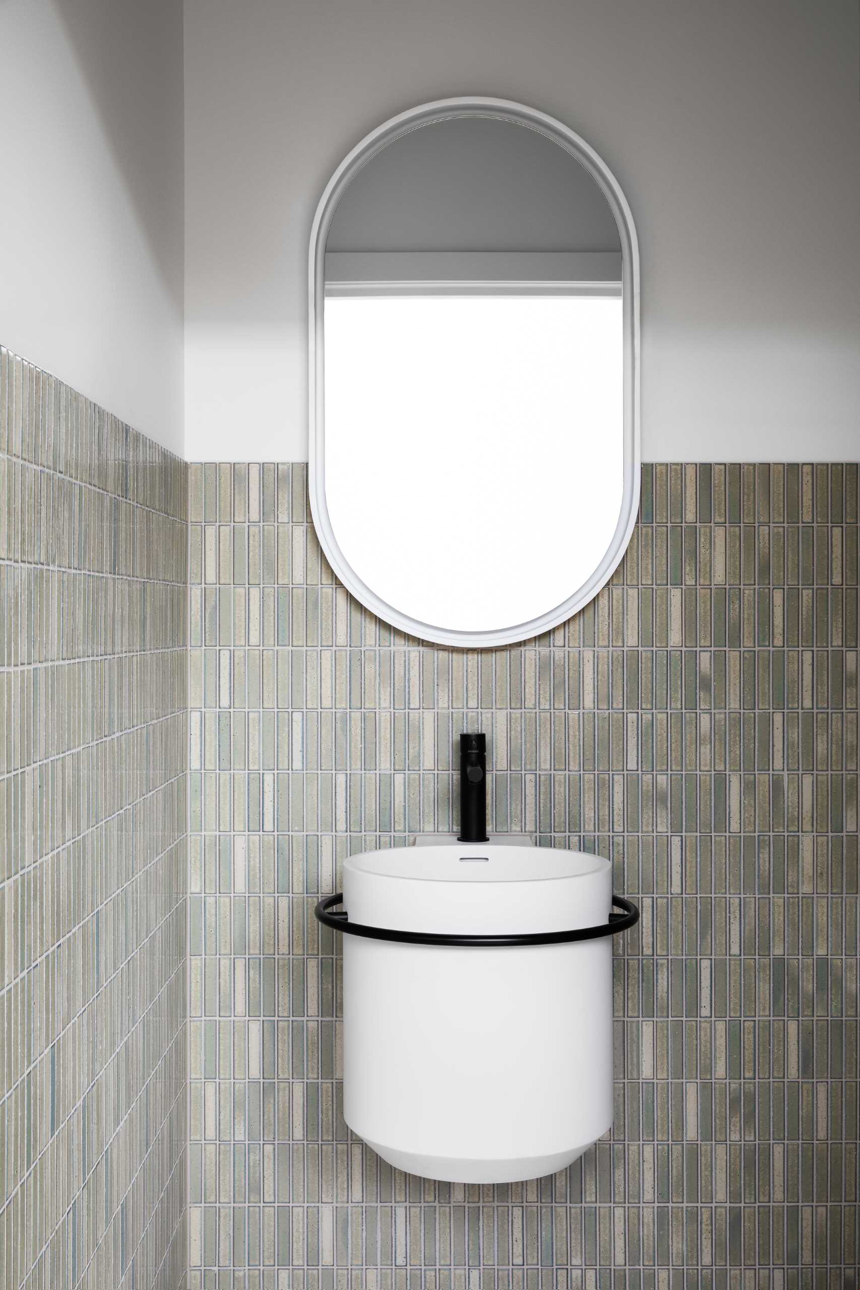 In this powder room, a floating basin is mounted below the mirror and has small rectangular tiles that cover the lower part of the wall.