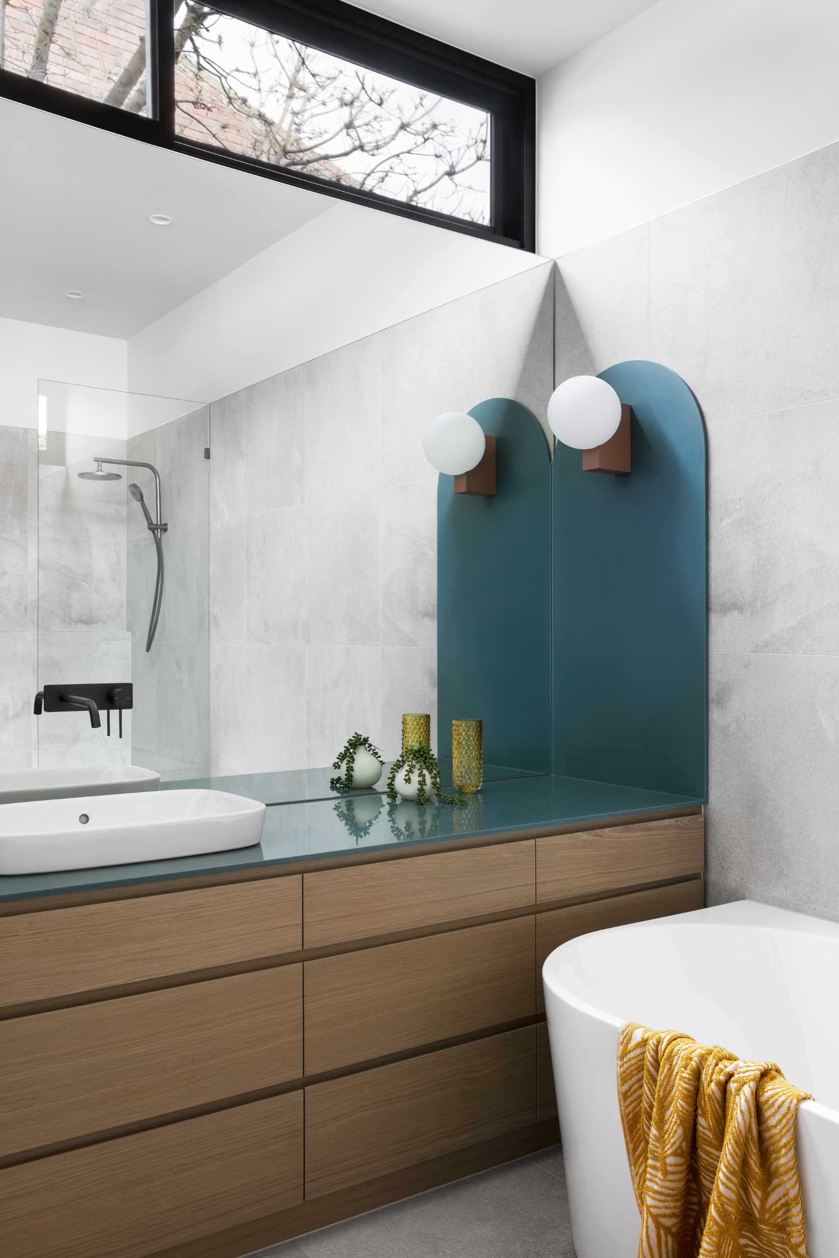 A modern bathroom with a large mirror, teal countertop, wood vanity, and a walk-in shower.
