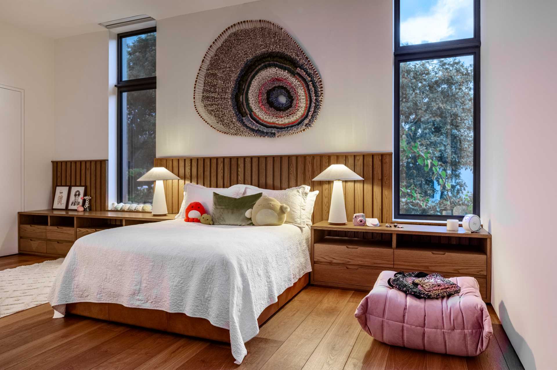 This modern bedroom is furnished with a Togo pouf by Michel Ducaroy and a woven artwork by Tammy Kanat.