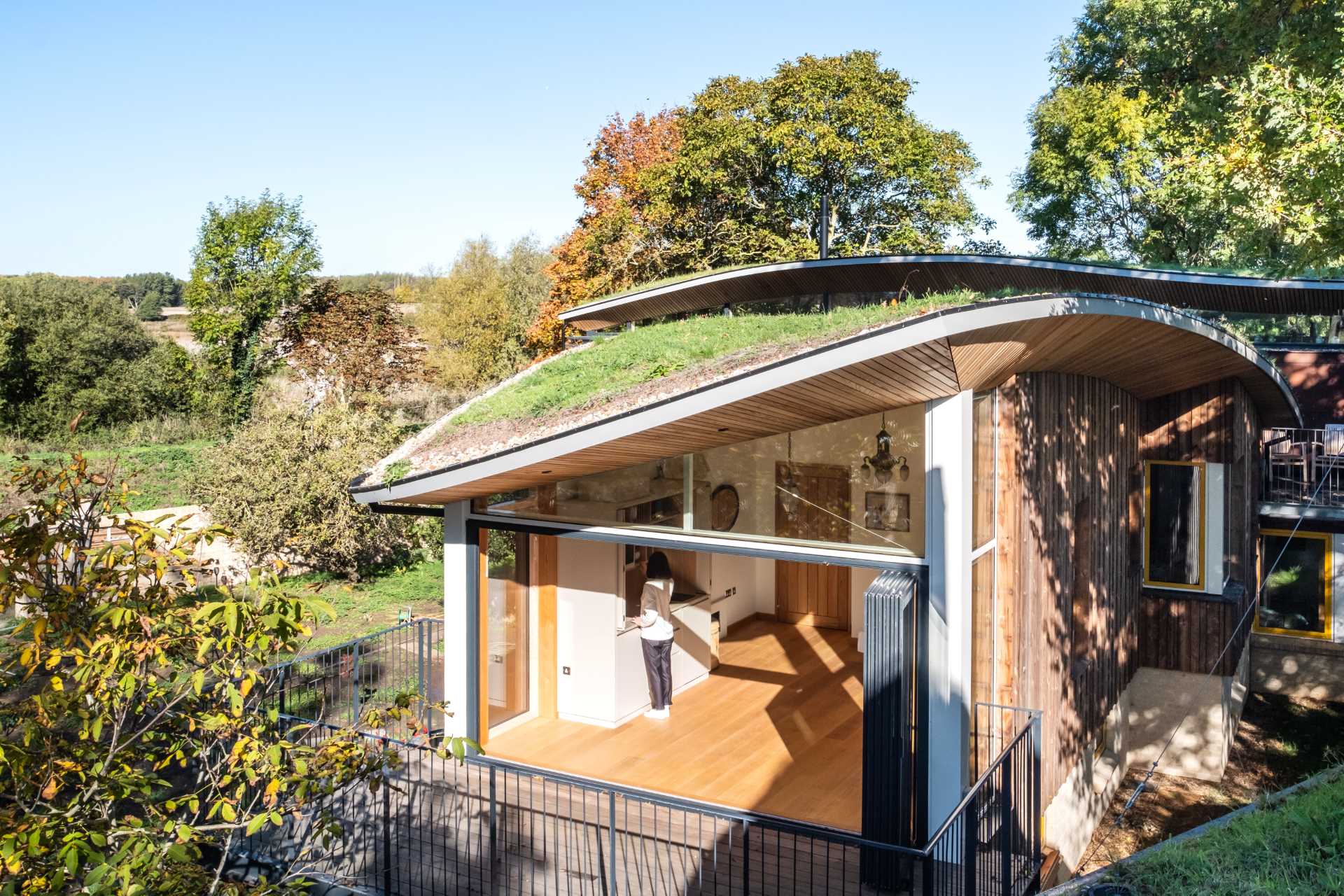 A modern cabin with overhanging wood-lined eaves and curved green roofs.