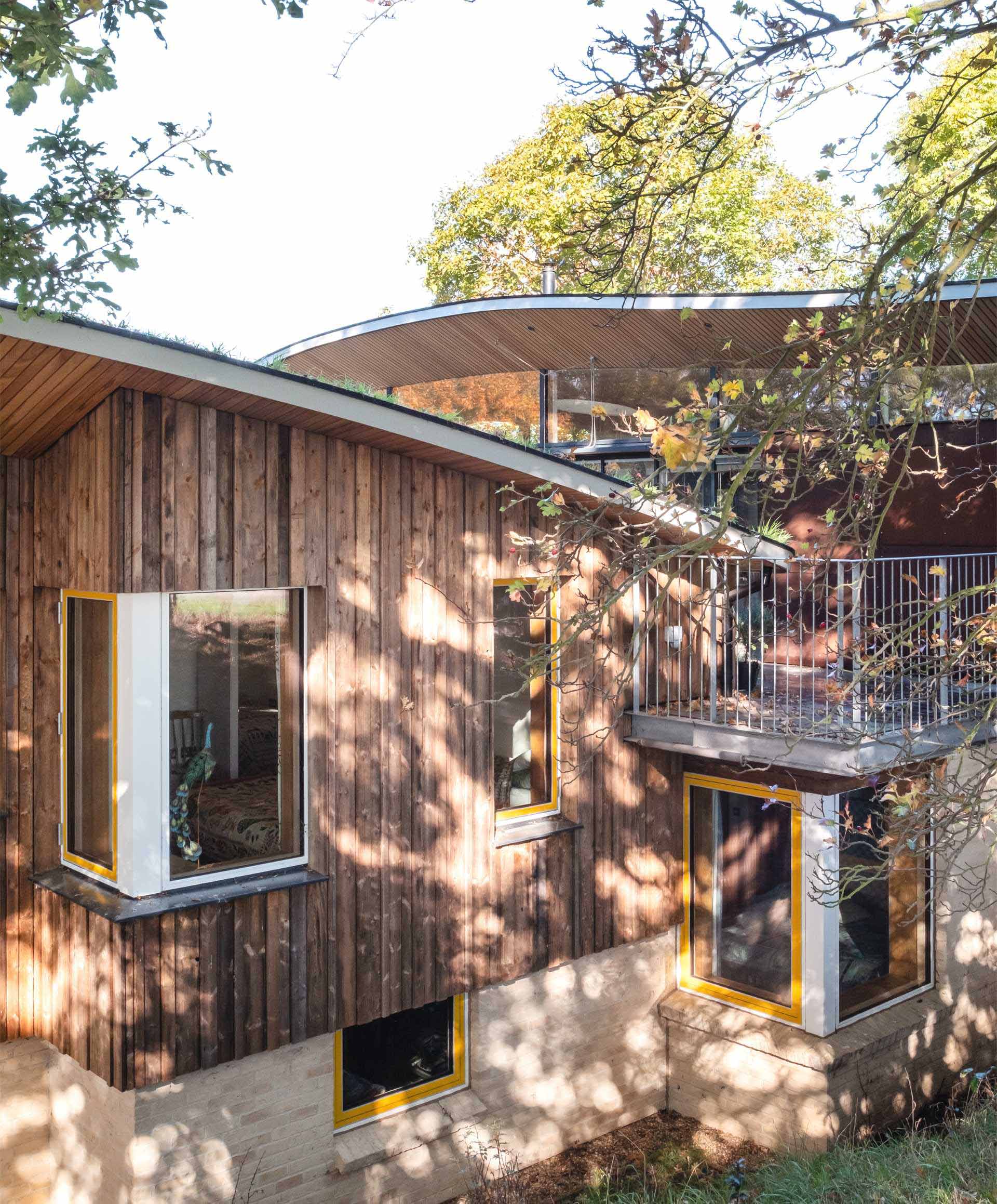 A modern cabin with overhanging wood-lined eaves and curved green roofs.