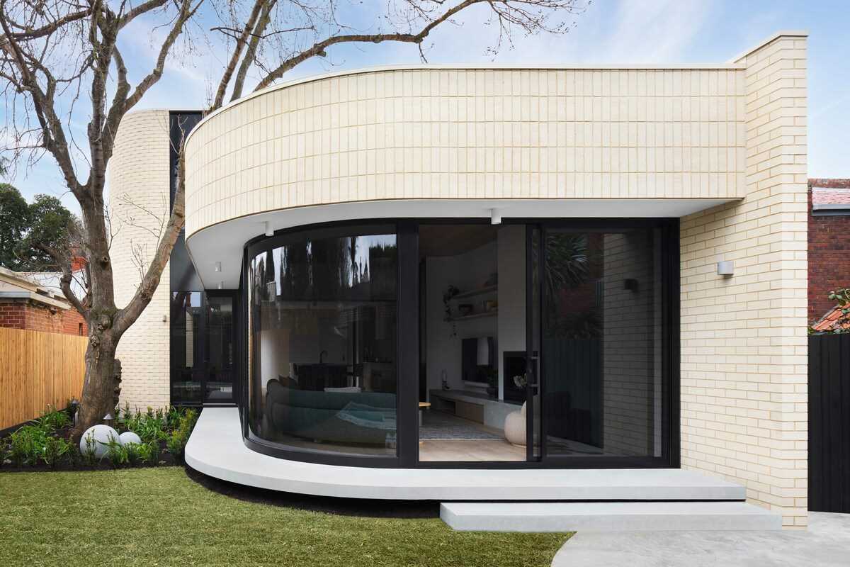 A modern light brick rear addition with a curved design and openings that connect the interior with outdoor spaces.