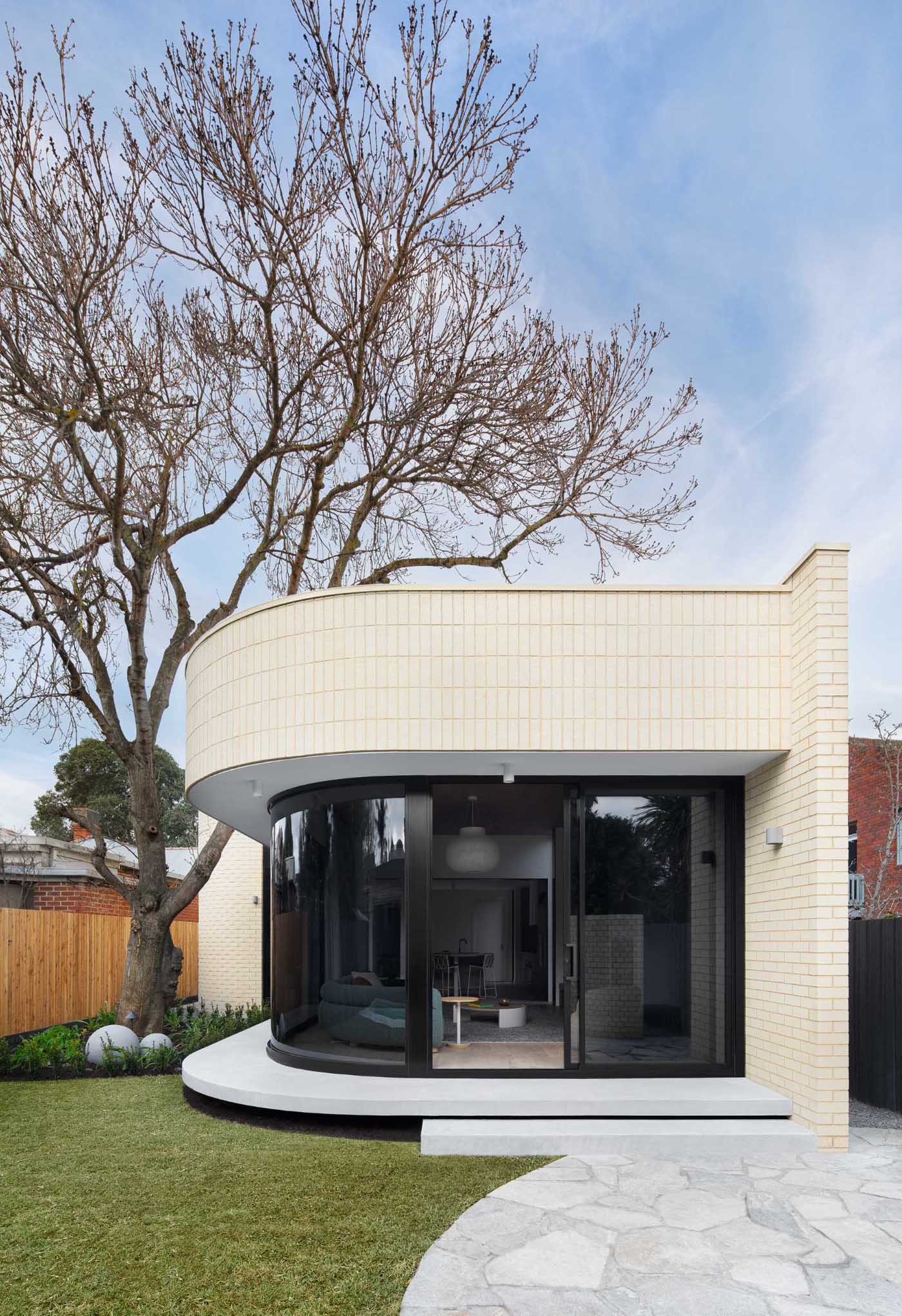 A modern light brick rear addition with a curved design and openings that connect the interior with outdoor spaces.