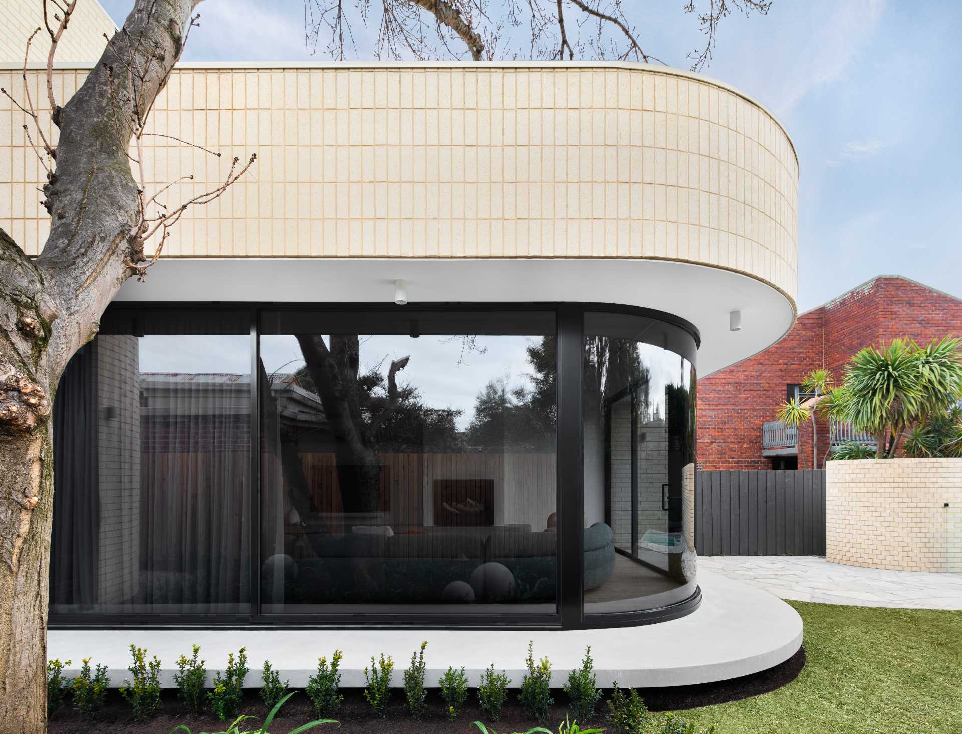 A modern light brick rear addition with a curved design and openings that connect the interior with outdoor spaces.