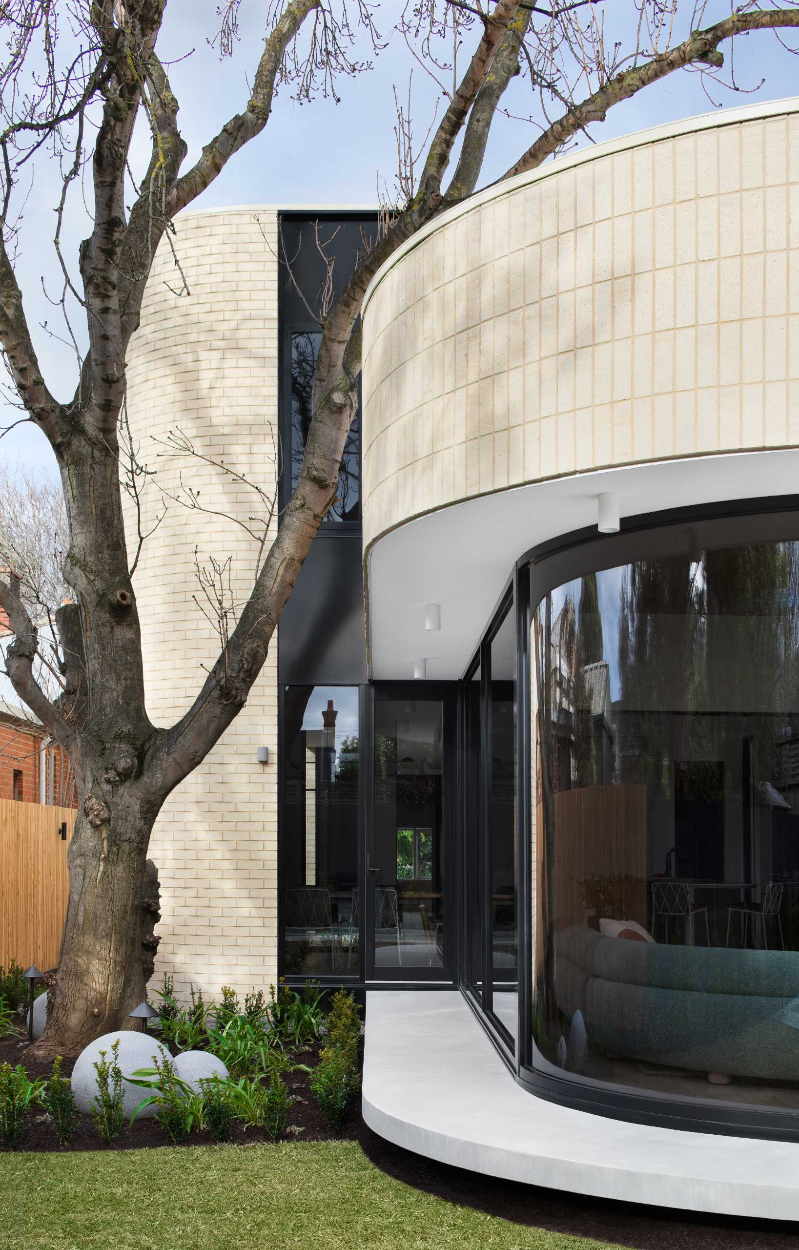 A modern light brick rear addition with a curved design and openings that connect the interior with outdoor spaces.