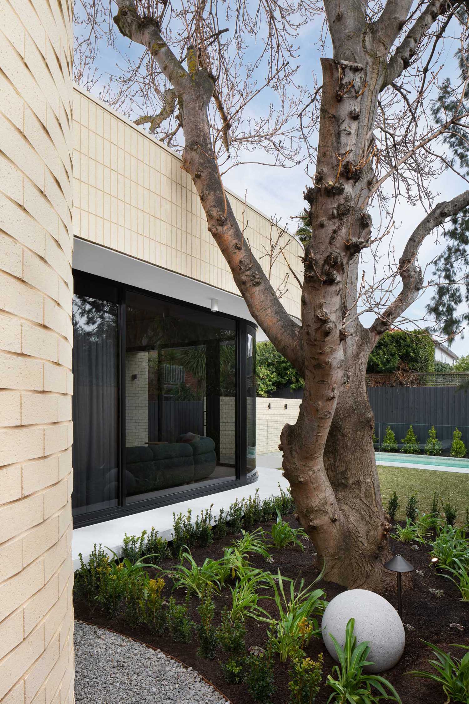 A modern light brick rear addition with a curved design and openings that connect the interior with outdoor spaces.