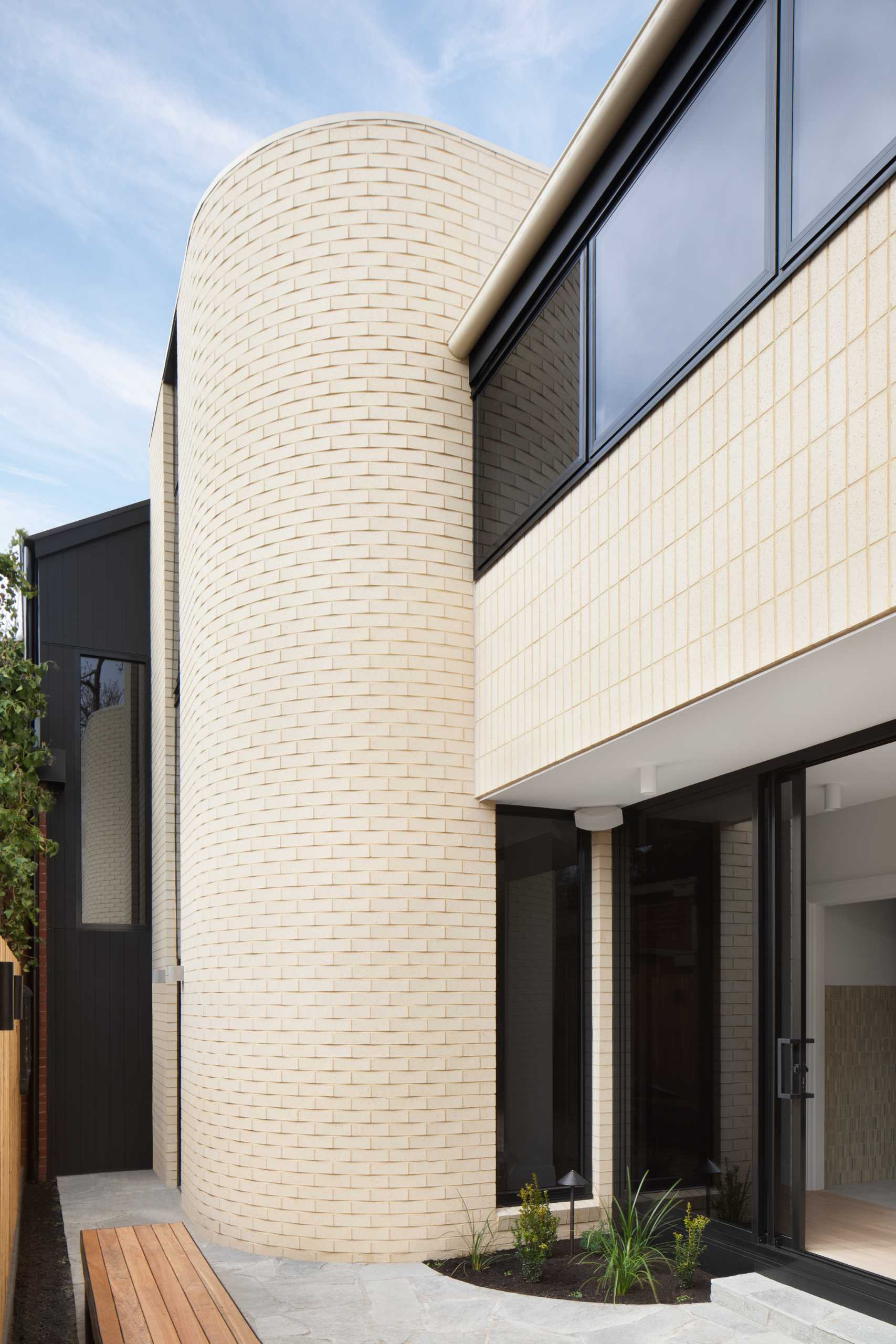 A modern light brick rear addition with a curved design and openings that connect the interior with outdoor spaces.