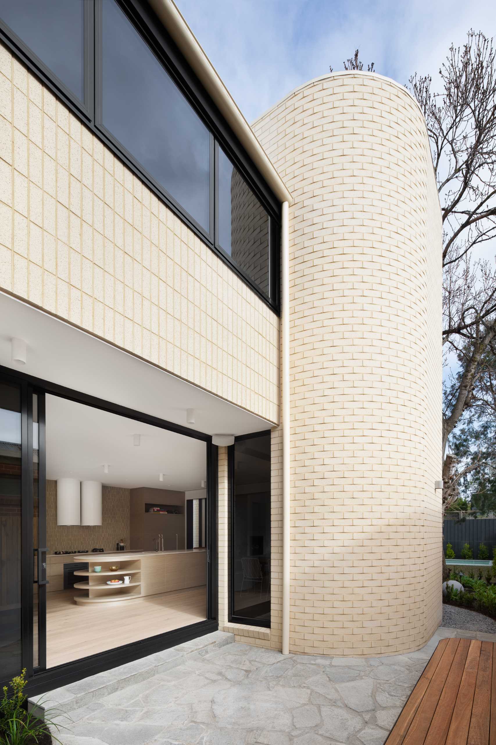 A modern light brick rear addition with a curved design and openings that connect the interior with outdoor spaces.