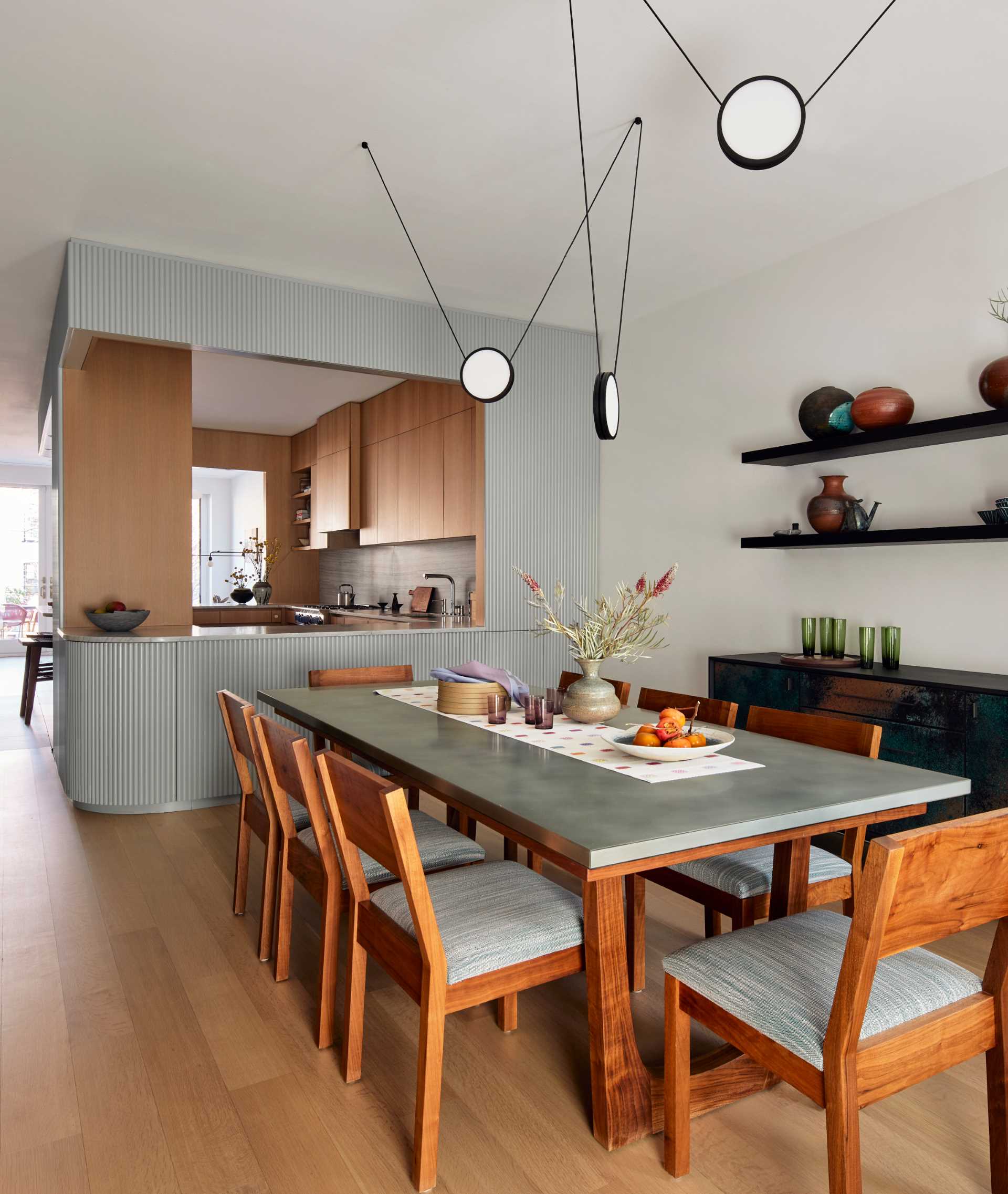 In this contemporary dining area, a pendant by Anony zig zags over the dining table, framing a display of the client’s ceramic vessels.