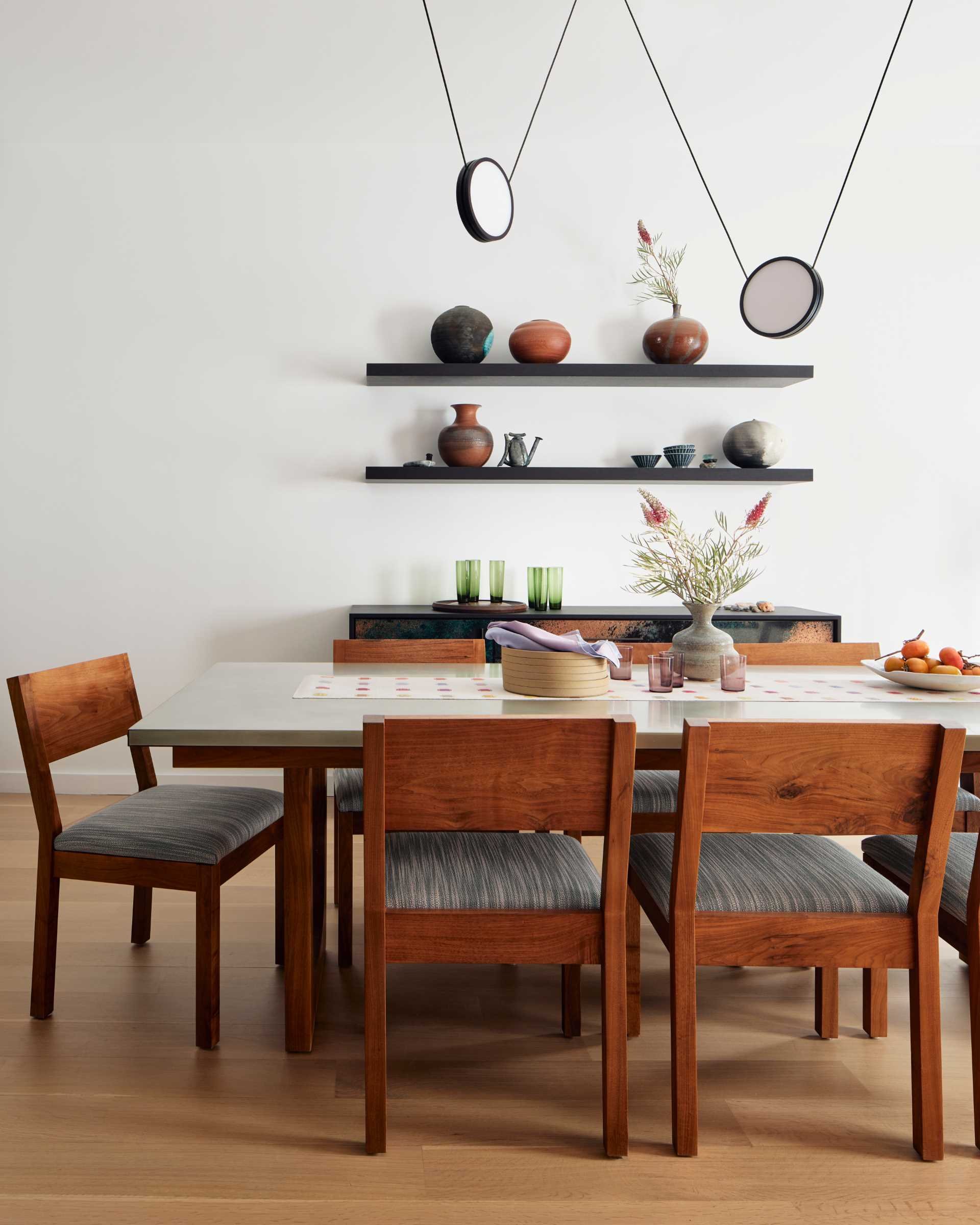 In this contemporary dining area, a pendant by Anony zig zags over the dining table, framing a display of the client’s ceramic vessels.