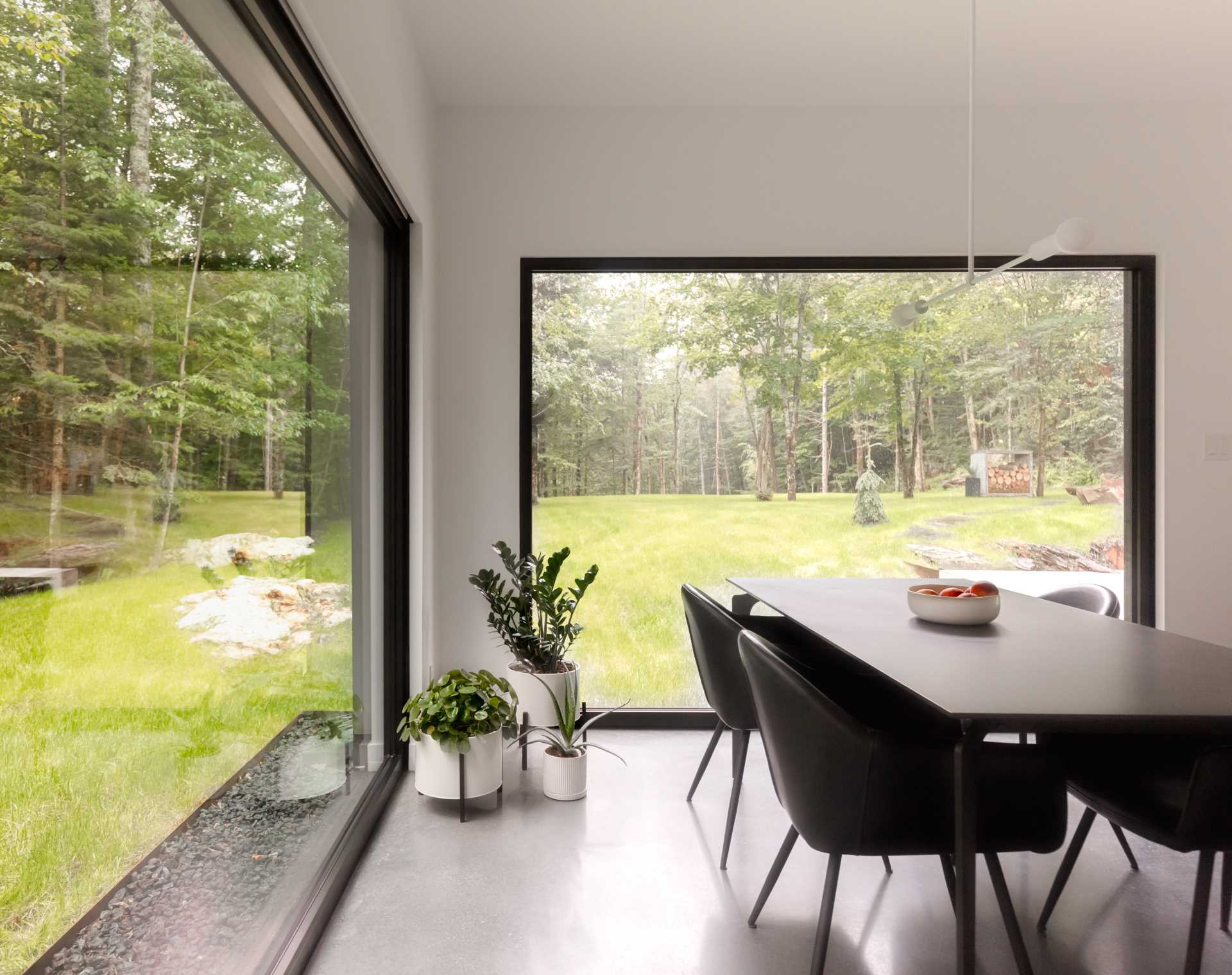 A dining room with large black-framed picture windows and white walls.