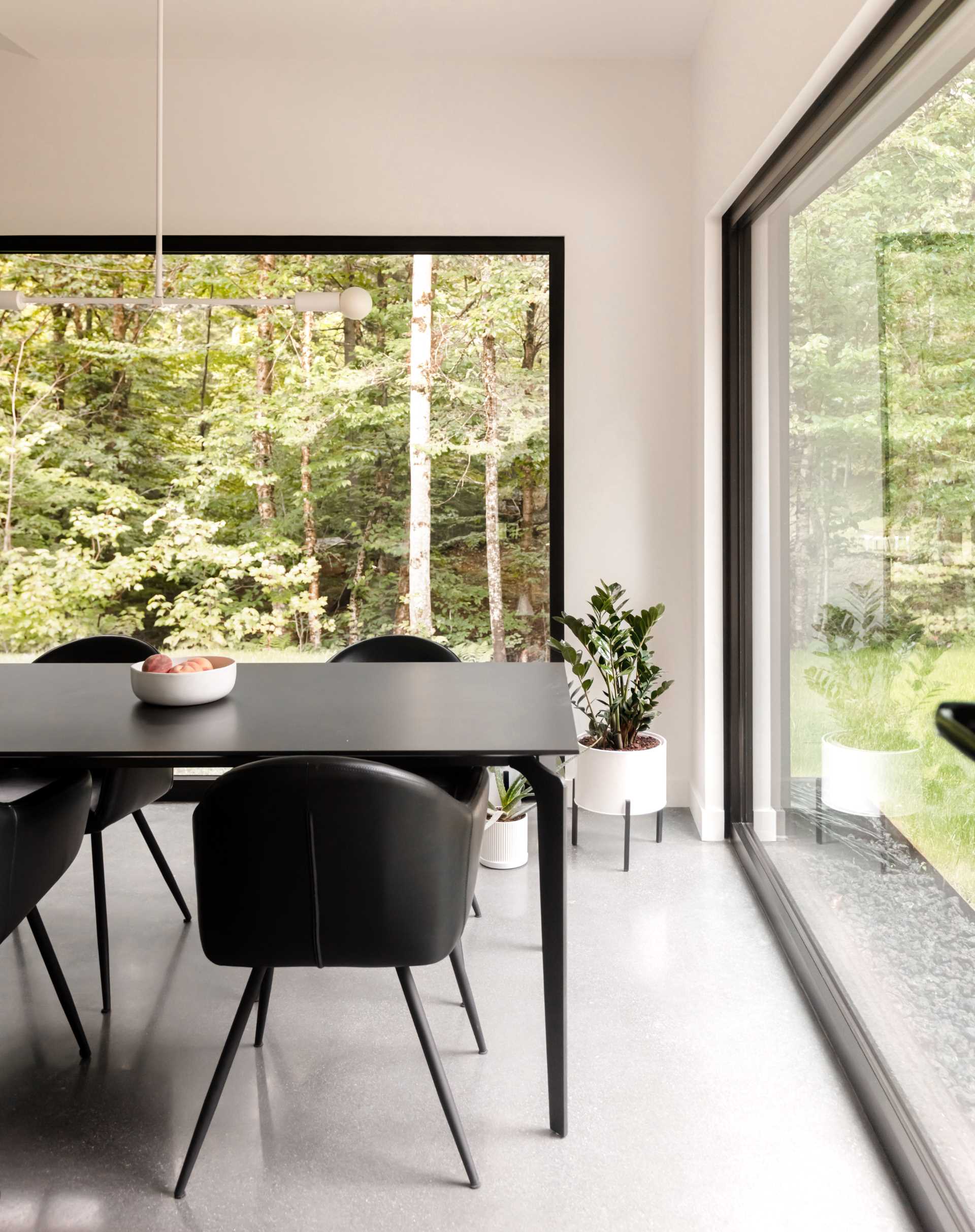 A dining room with large black-framed picture windows and white walls.