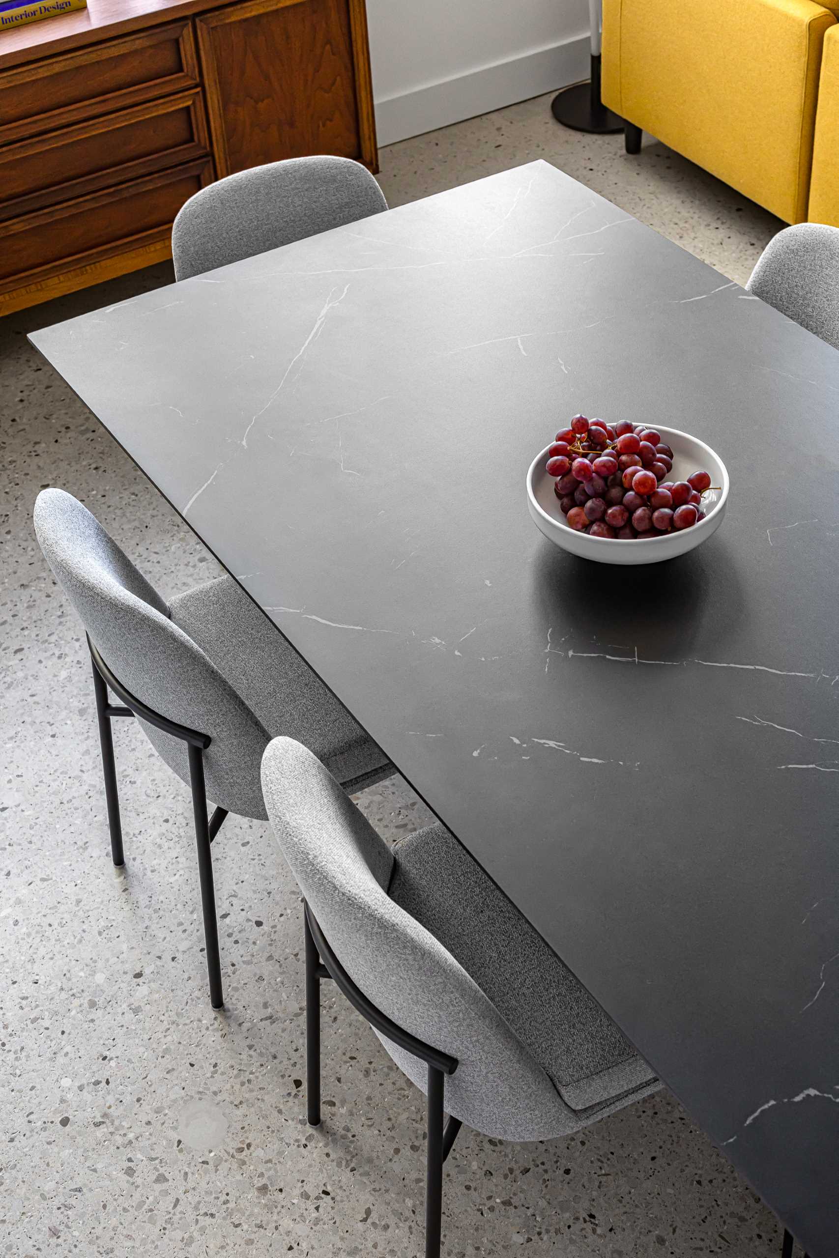 This open-plan dining area in a loft apartment has been furnished with a black ceramic dining table with dramatic veins which is surrounded by more subtle grey upholstered chairs. 