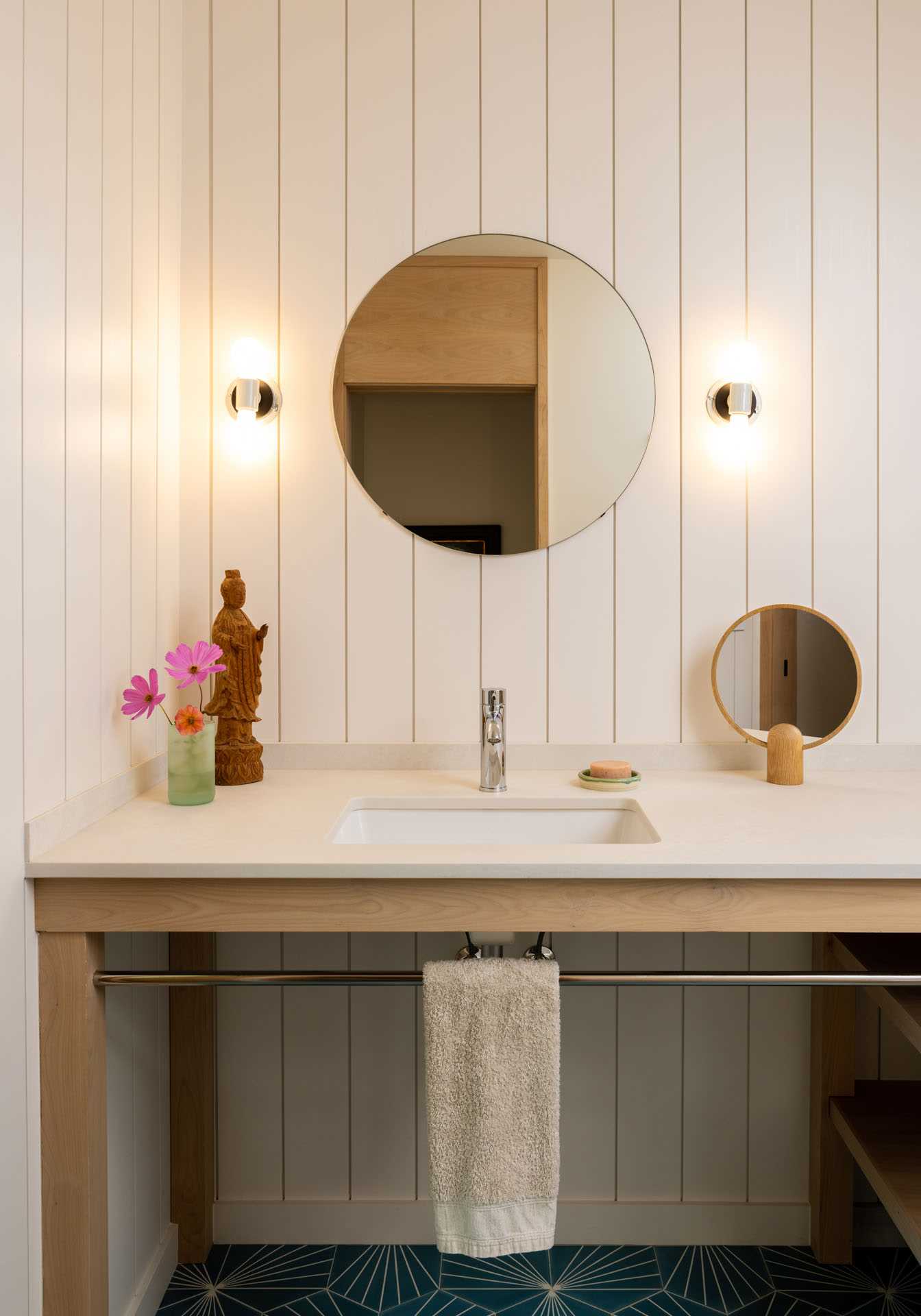 A contemporary farmhouse bathroom with a wood vanity and round mirror.