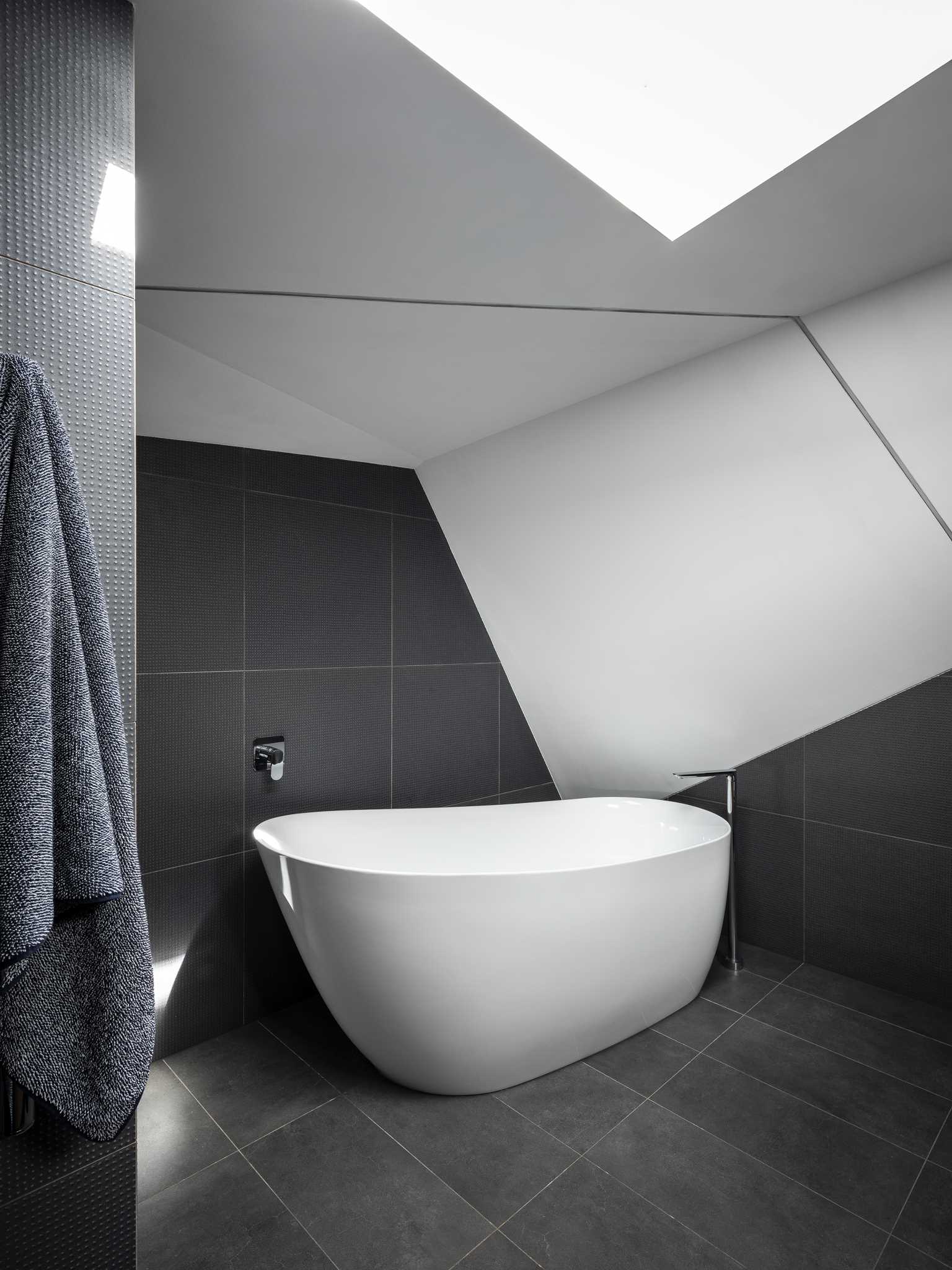 In this bathroom, grey tiles partially installed with a diagonal design add visual interest and are paired with white walls and a wood vanity. A skylight helps to keep the bathroom bright.