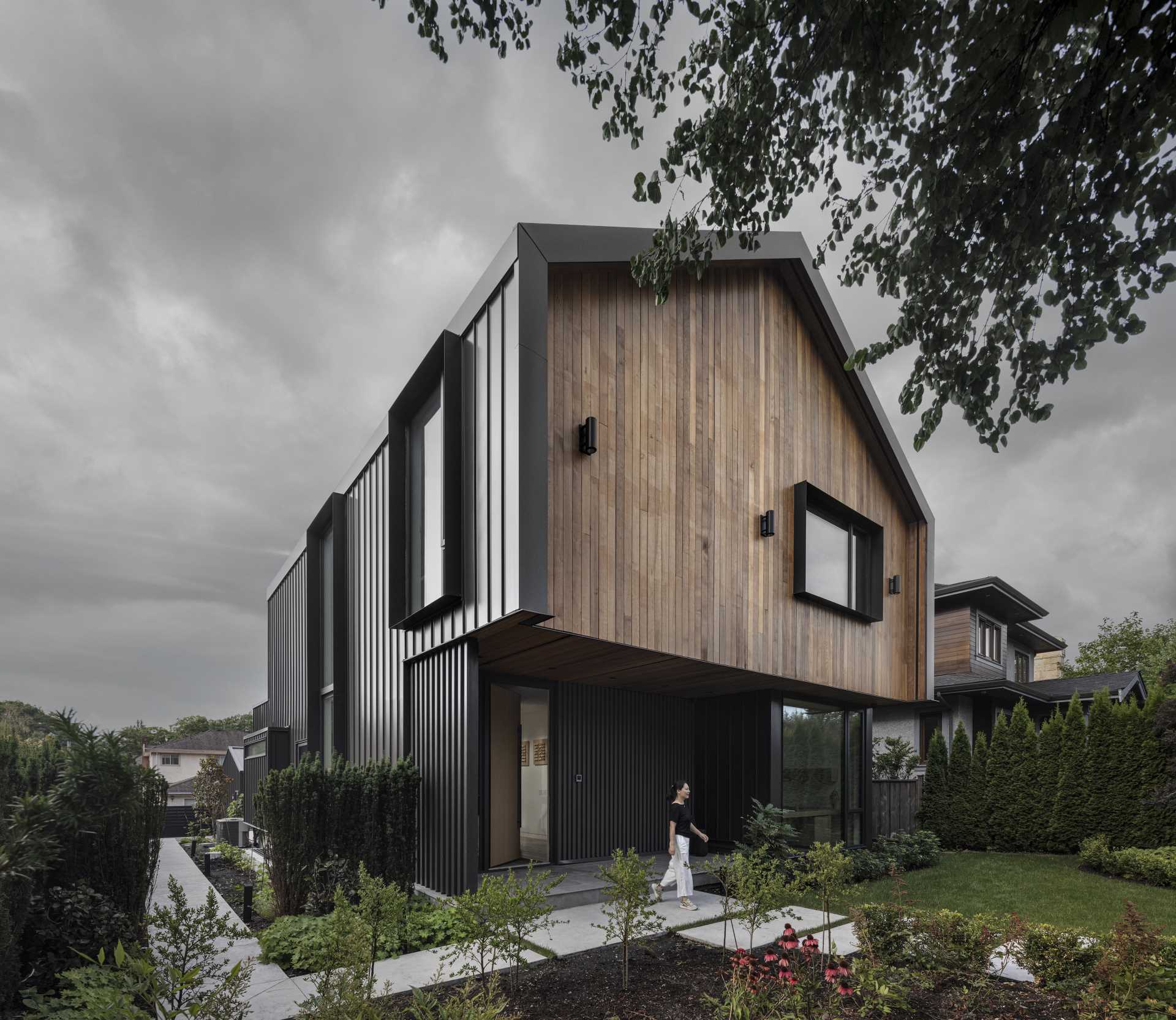 This modern home has a prominent gable form that floats atop the main level of the house, creating a cantilevered cover over a large recessed entry patio.