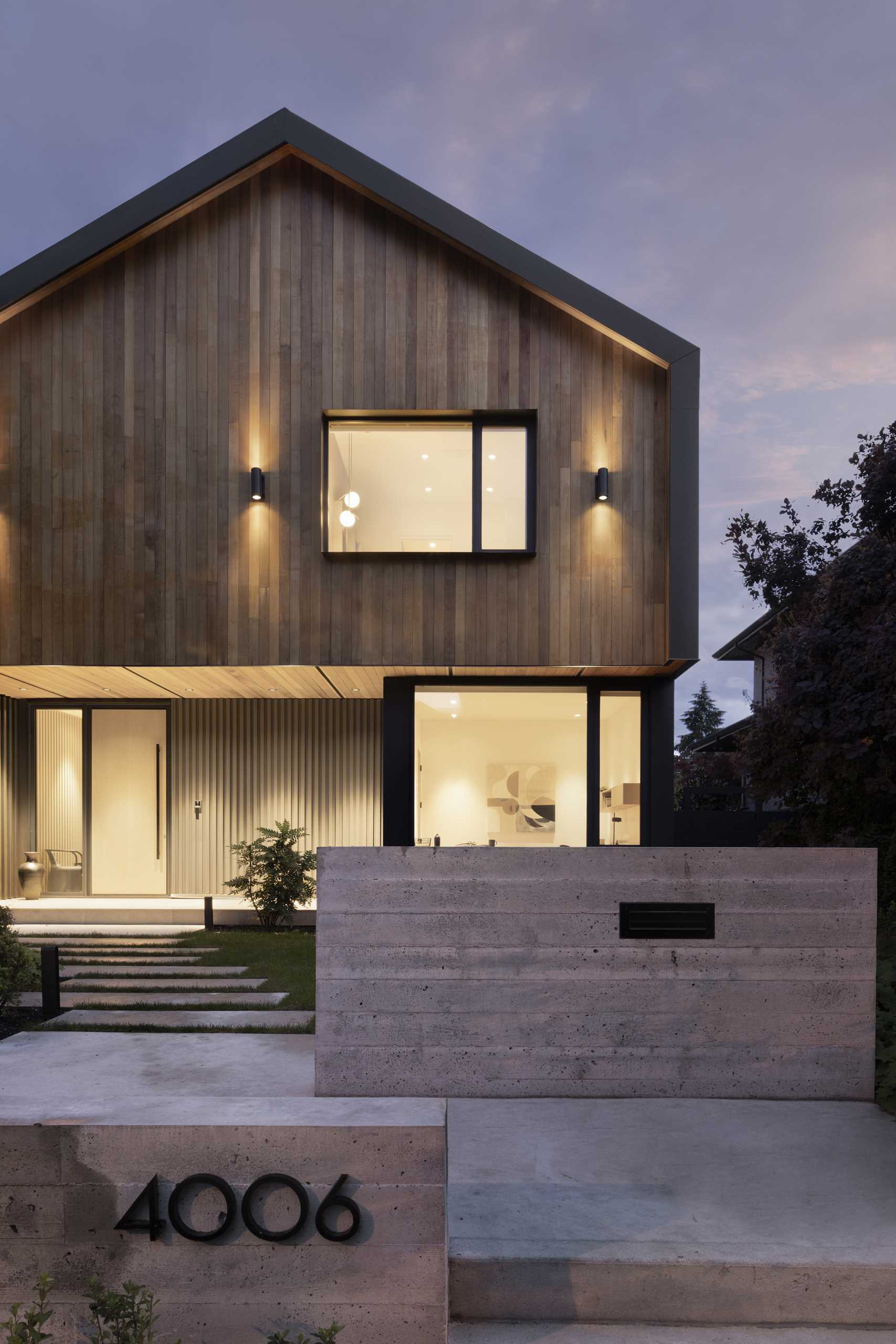 This modern home has a prominent gable form that floats atop the main level of the house, creating a cantilevered cover over a large recessed entry patio.