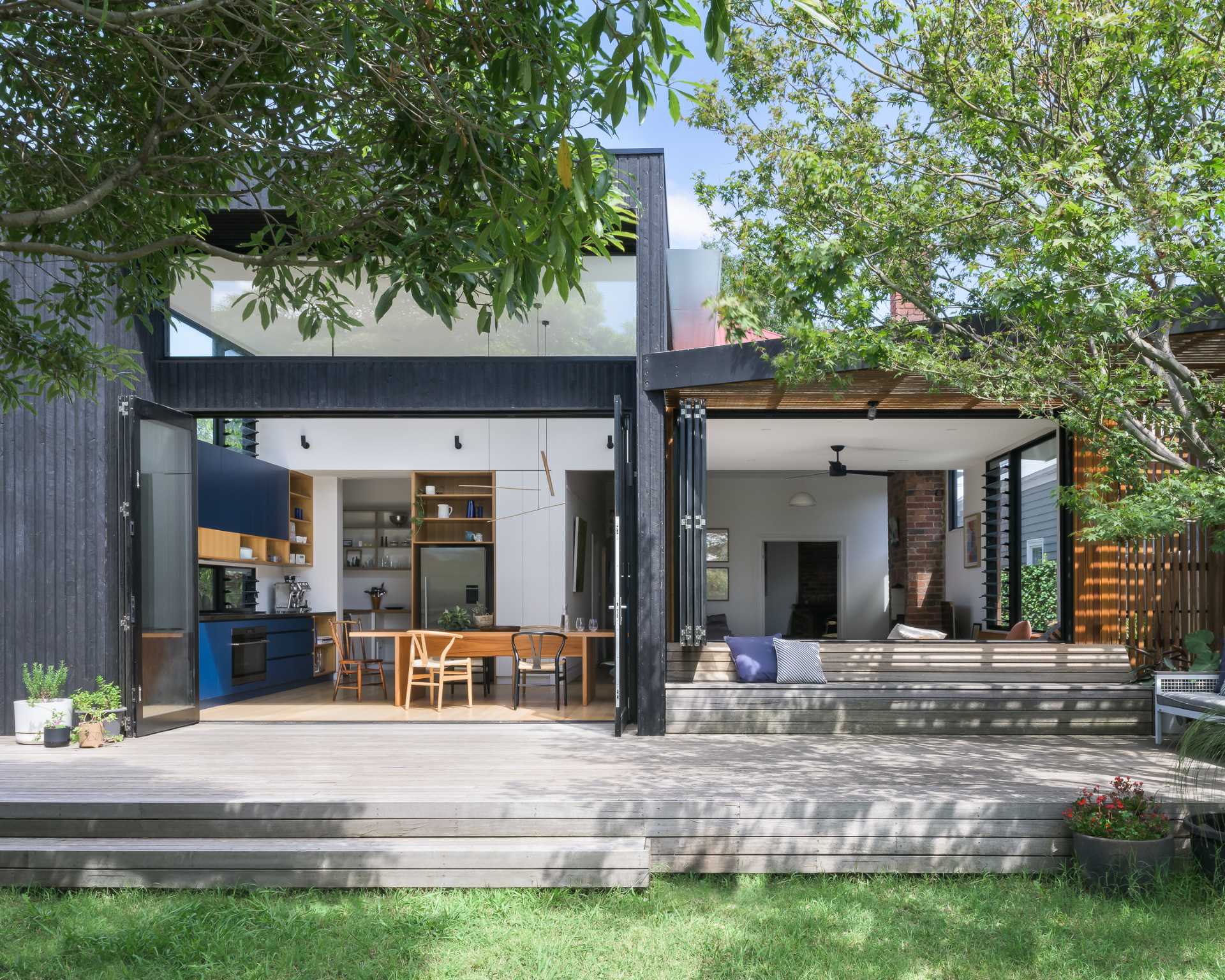 This modern deck has been designed with a shaded area that's home to built-in seating and a couch, as well as bi-fold doors and windows that connect the interior to the outdoors.