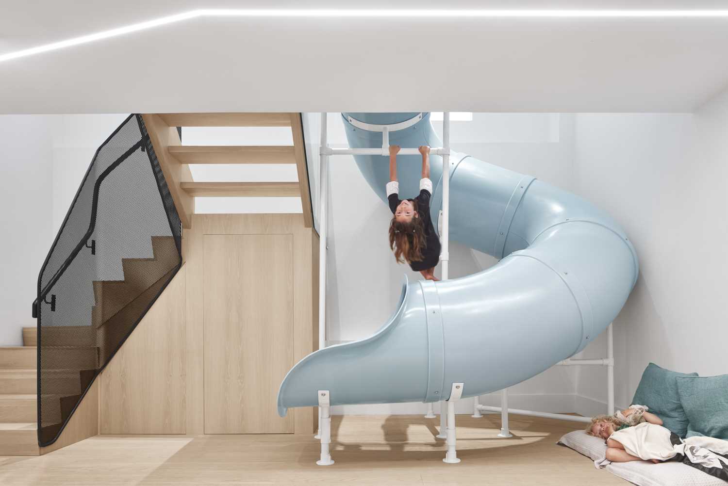 A modern house with a slide and stairs, that connects the main floor with the lower floor that houses a playroom, three kids bedrooms, and a guest room.