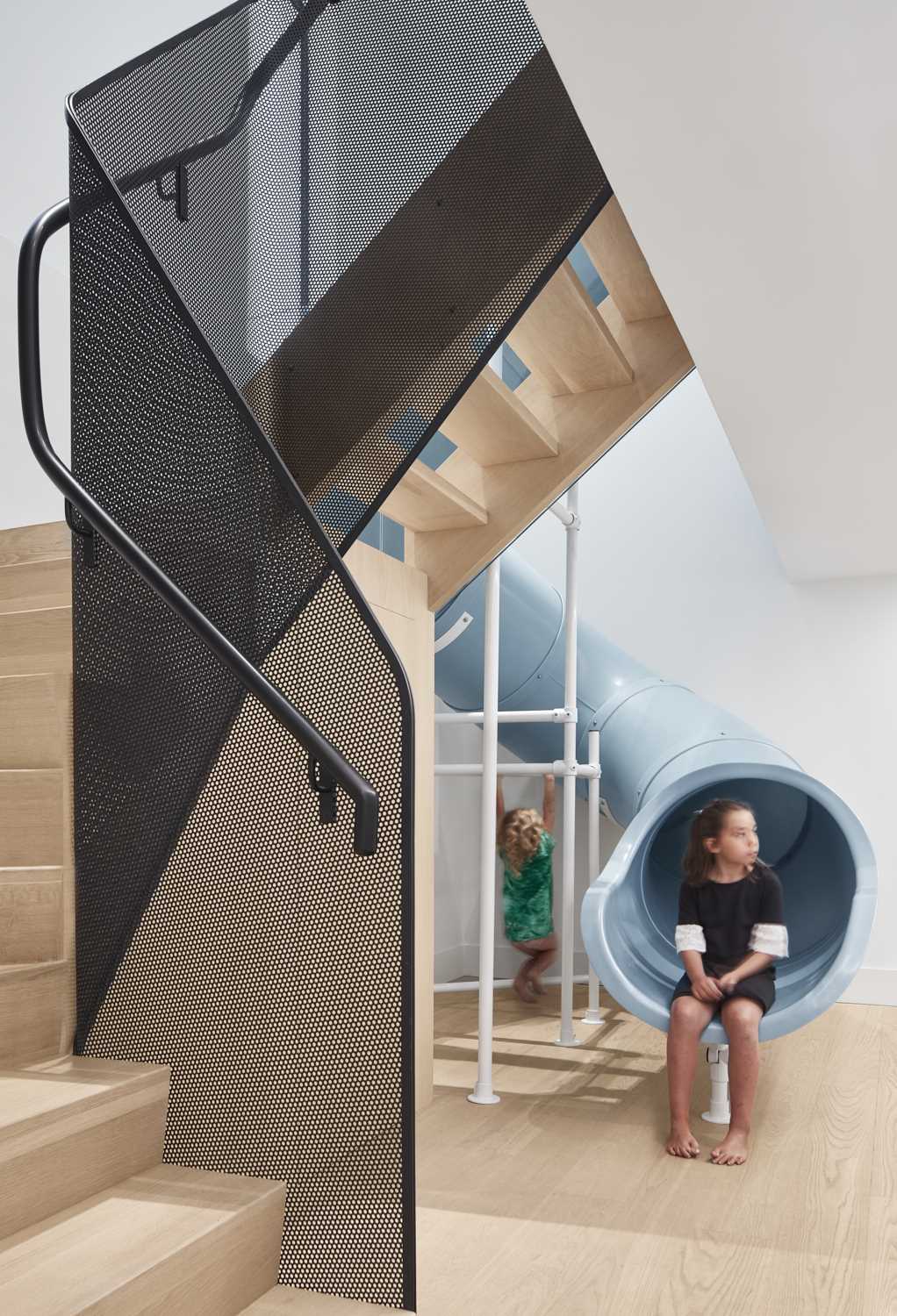 A modern house with a slide and stairs, that connects the main floor with the lower floor that houses a playroom, three kids bedrooms, and a guest room.