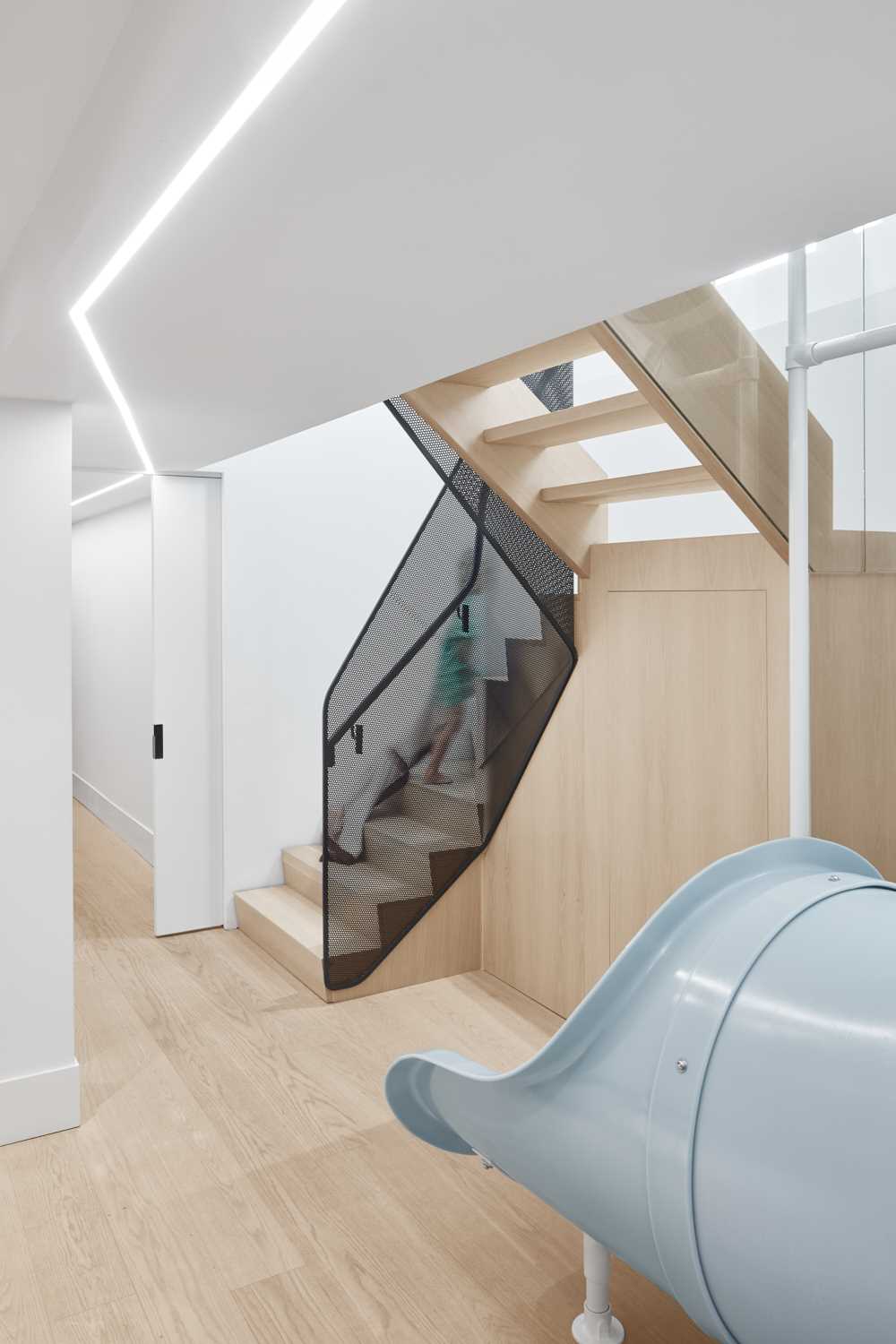 A modern house with a slide and stairs, that connects the main floor with the lower floor that houses a playroom, three kids bedrooms, and a guest room.