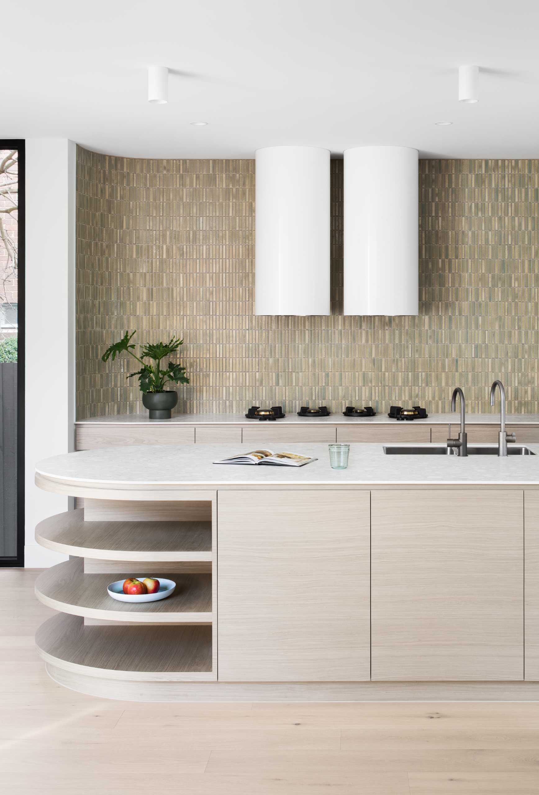 This modern kitchen features a tiled wall, wood cabinets, and an island with curved ends. One end is dedicated to seating, while the other has open shelving.