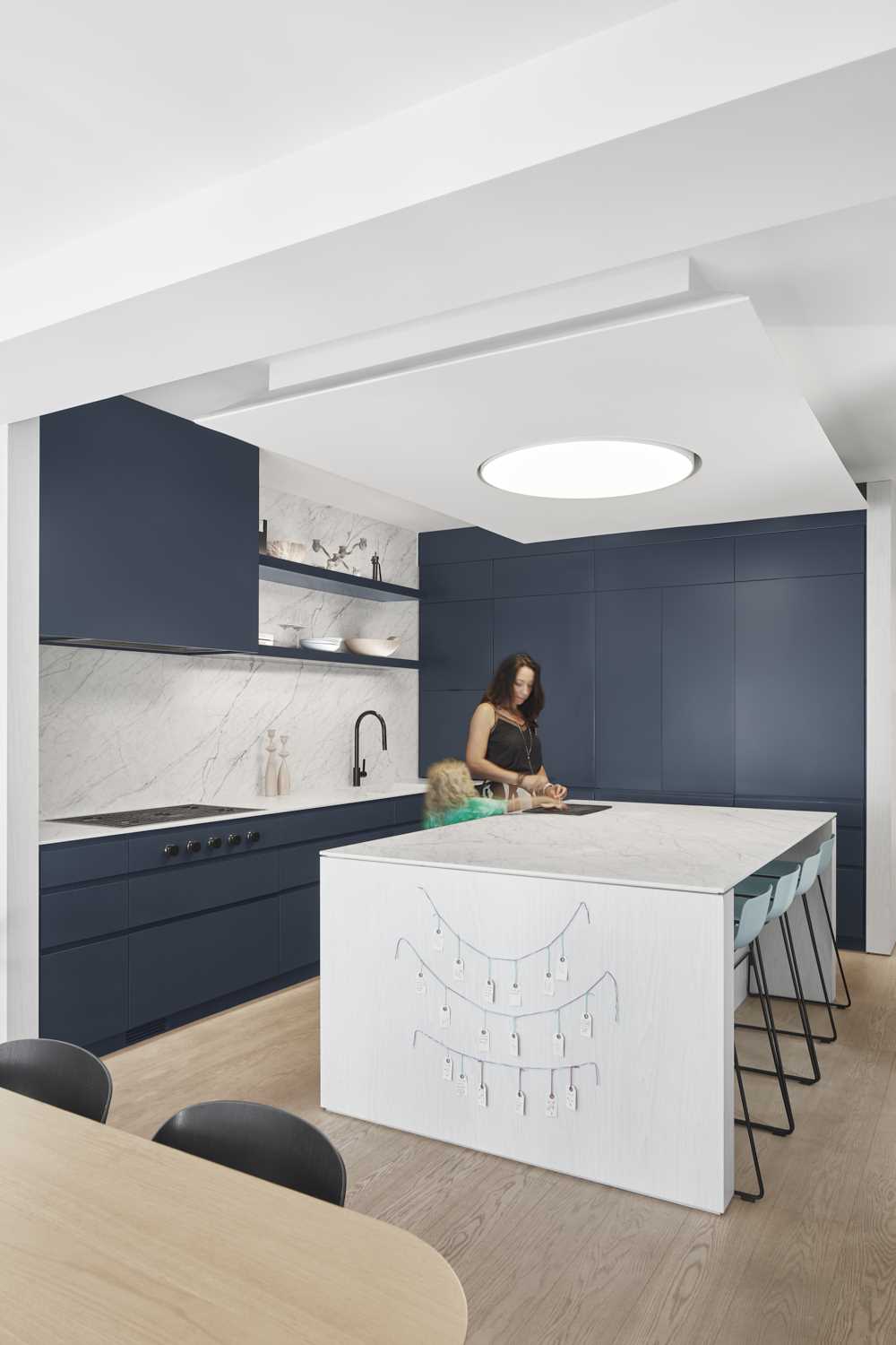 This modern kitchen includes minimalist dark cabinets, open shelving, light countertops, and an island.