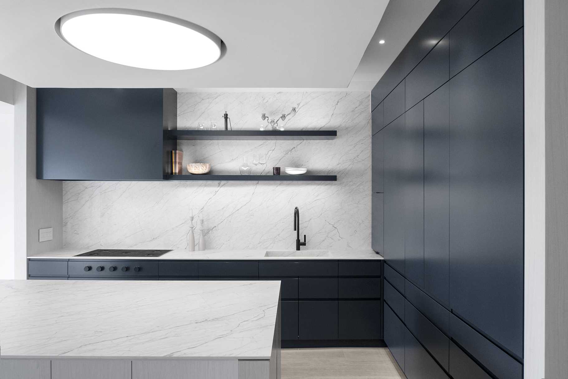 This modern kitchen includes minimalist dark cabinets, open shelving, light countertops, and an island.