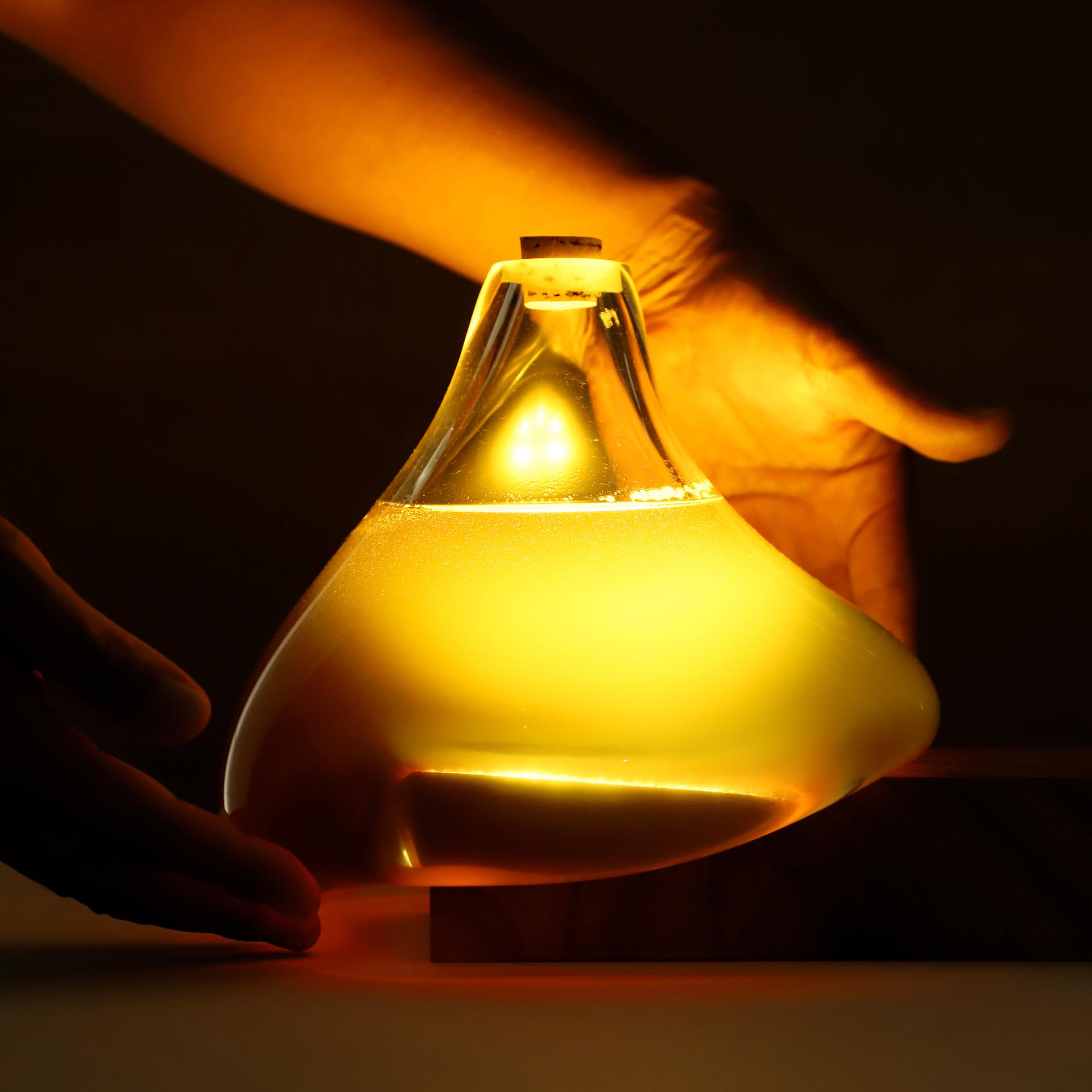 The Honey Drop Lighting is designed with a blown-glass container that's filled with honey and corked with a cork. The base is made of wood and has a rechargeable LED inside.