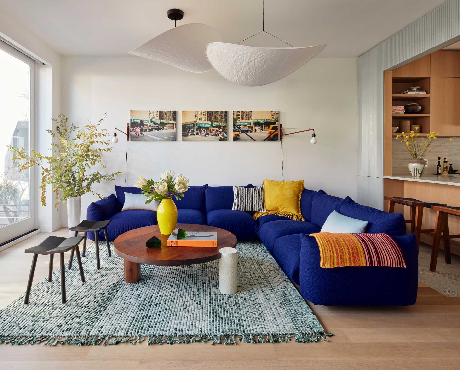 This modern living room looks out on the rear yard through floor-to-ceiling glass and includes a Marenco sectional in blue Kvadrat wool wraps, a coffee table by Hinterland Design, and a rug by Philippe Malouin.