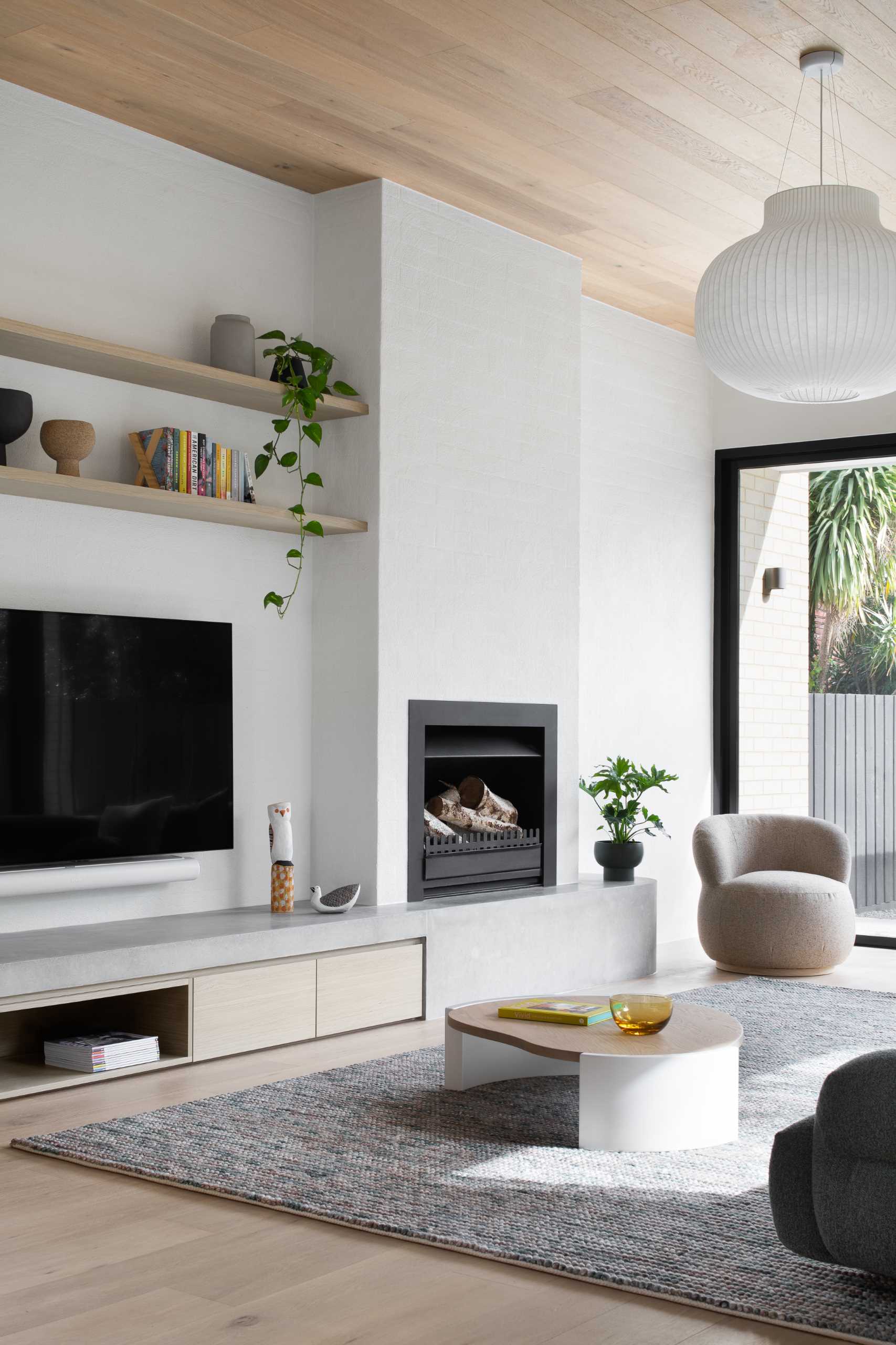 A modern living room with a curved wall, wood ceiling, fireplace, and a hearth that travels along the wall and includes a storage cabinet.