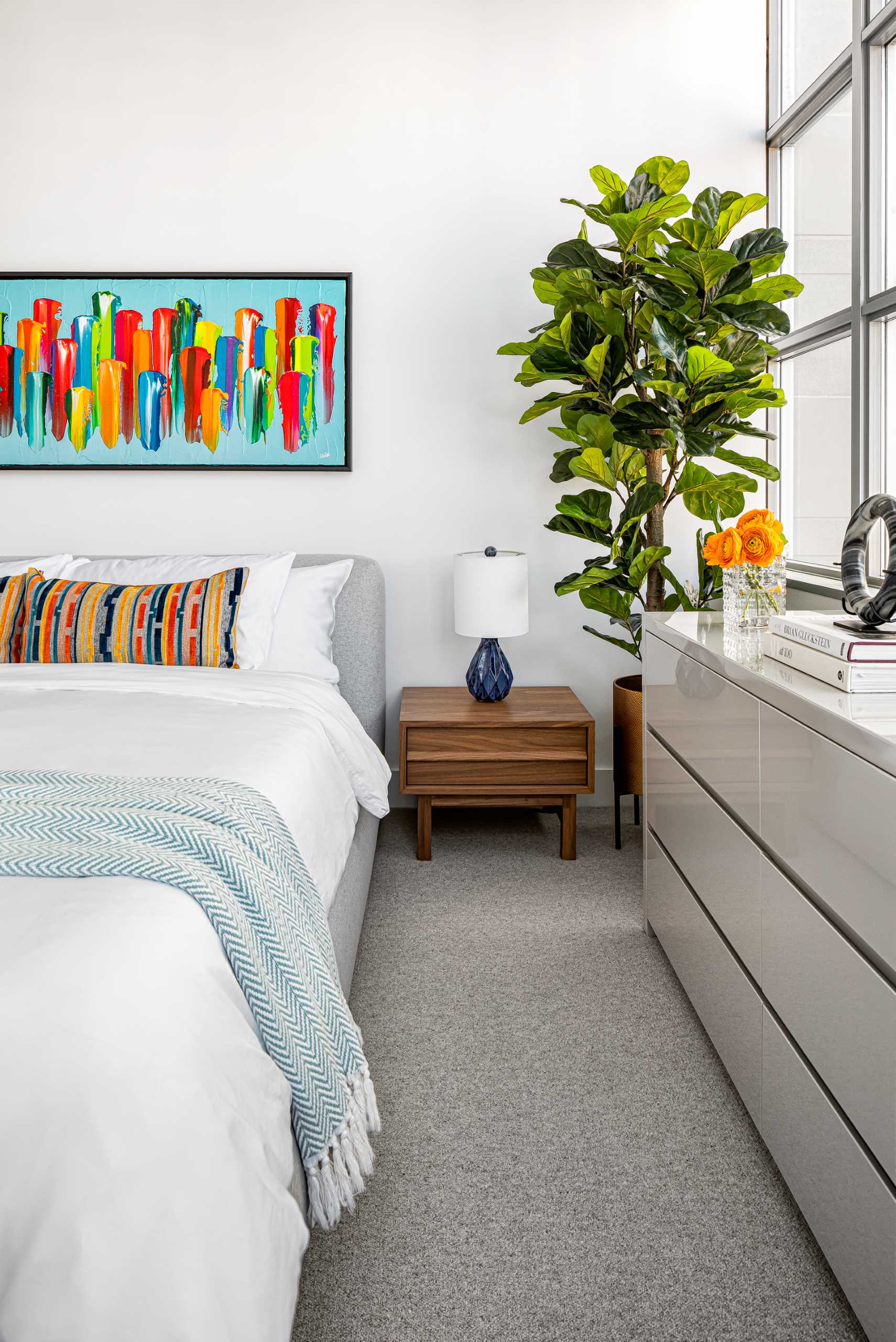 This contemporary primary bedroom in a loft apartment has a subtle color palette, with a large king bed in a soft grey wool fabric. 