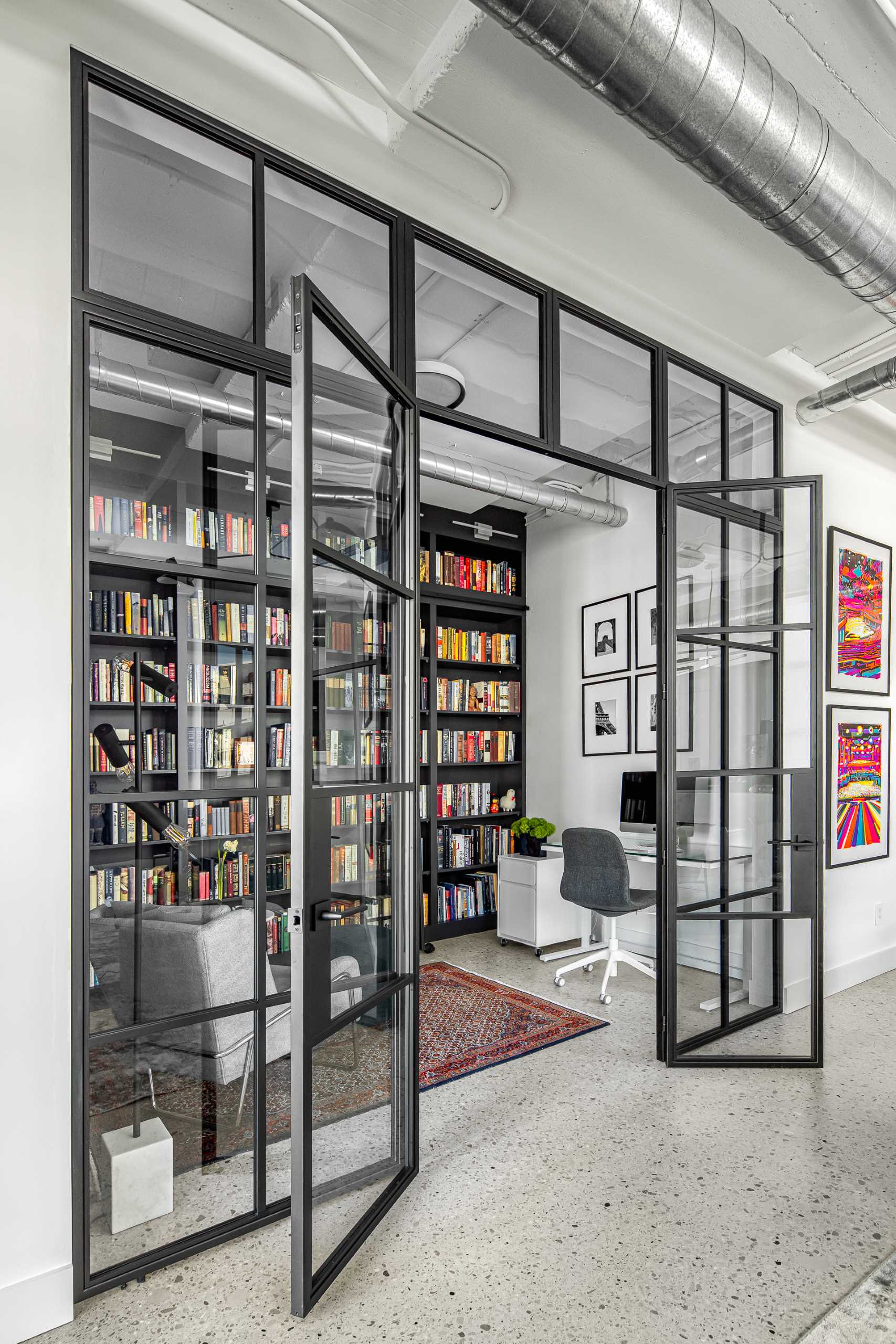 A modern home library enclosed behind a glass wall, has custom black shelving and a ladder to reach the upper shelves.
