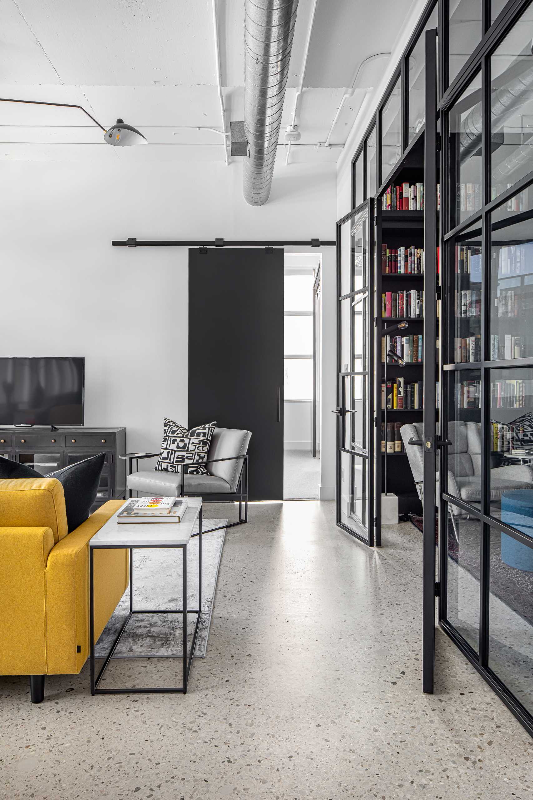 A modern home library enclosed behind a glass wall, has custom black shelving and a ladder to reach the upper shelves.