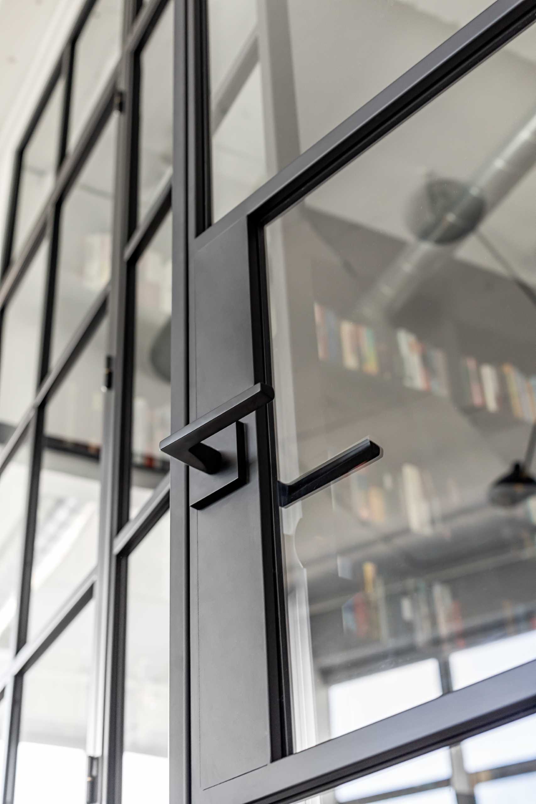 A modern home library enclosed behind a glass wall, has custom black shelving and a ladder to reach the upper shelves.