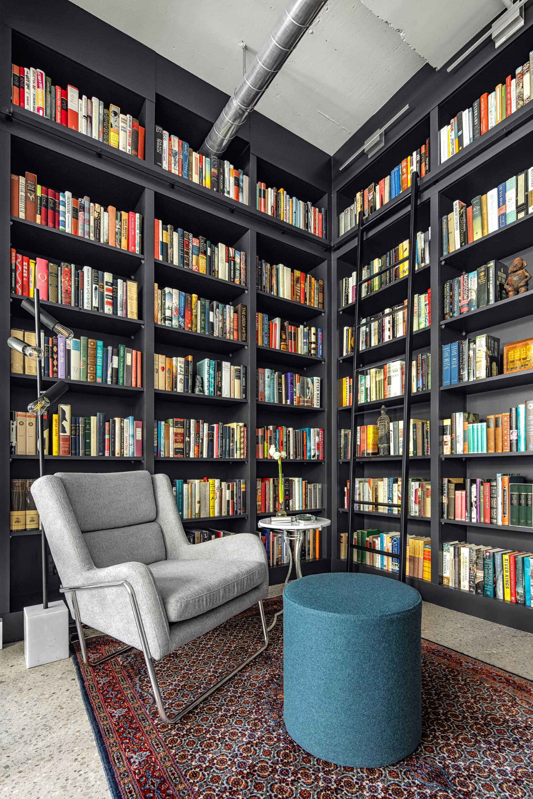 A modern home library with custom black shelving and a ladder to reach the upper shelves.