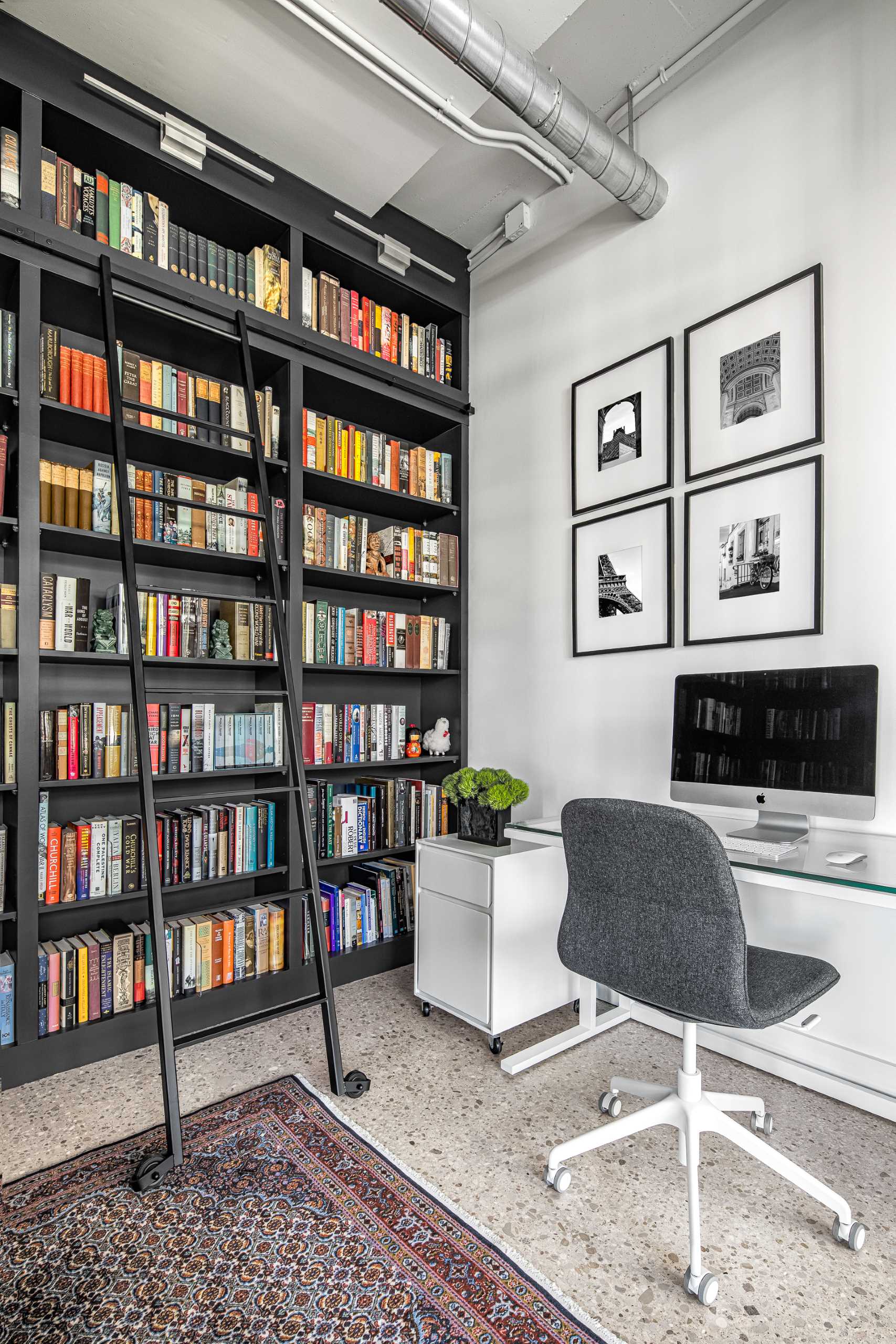 The home office in a library is positioned against an empty wall, and has art with black frames to match the shelving.