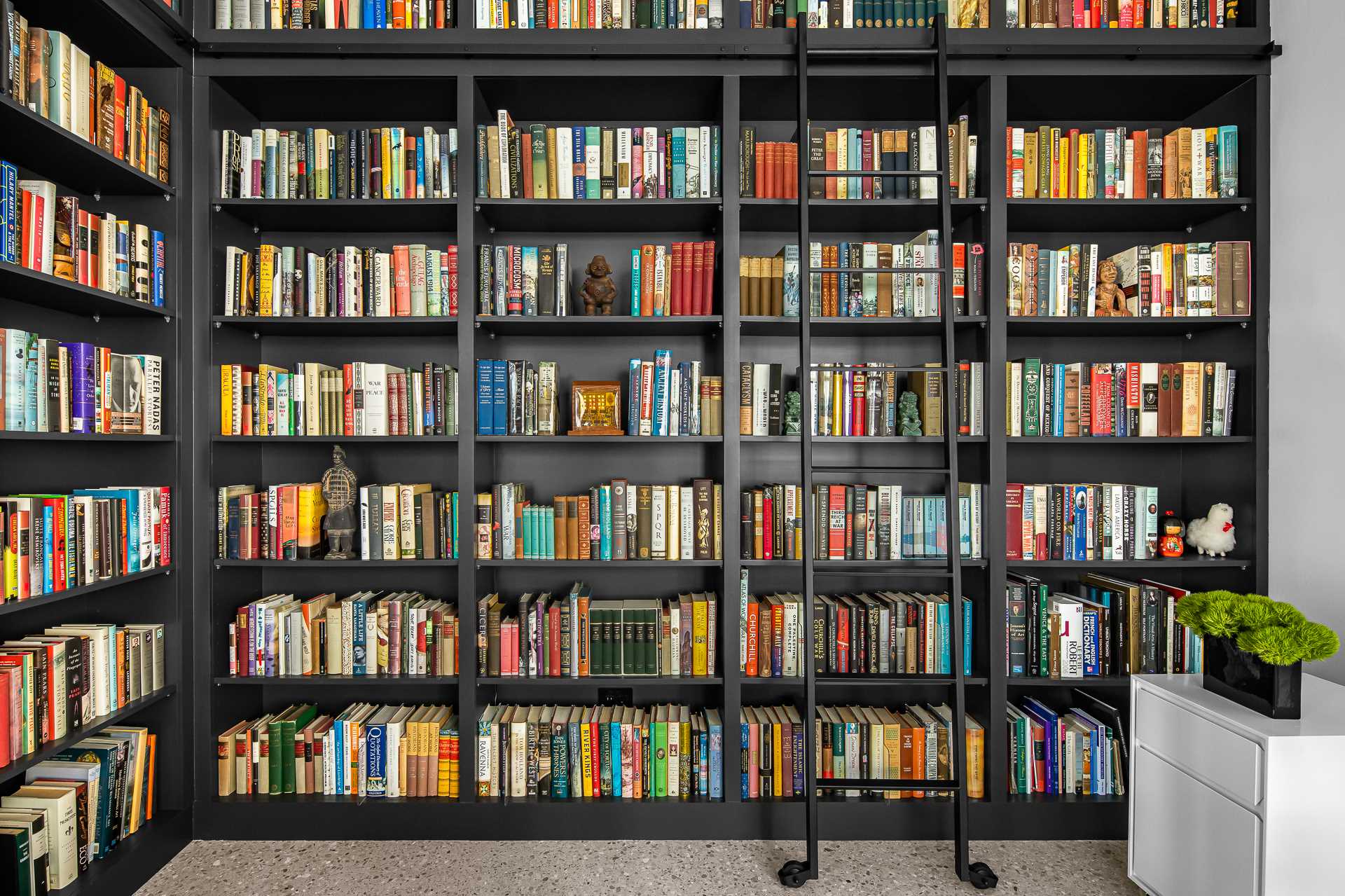 A modern library in a loft apartment includes a ladder to reach the top of the shelves.