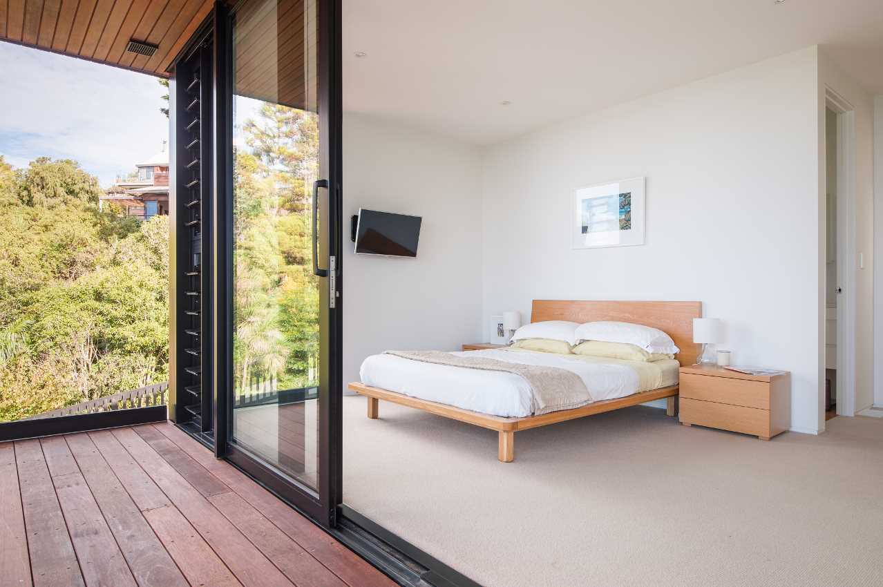 A modern bedroom has a sliding glass door to connect it to the balcony, while inside, the furniture has been kept minimal in its design.