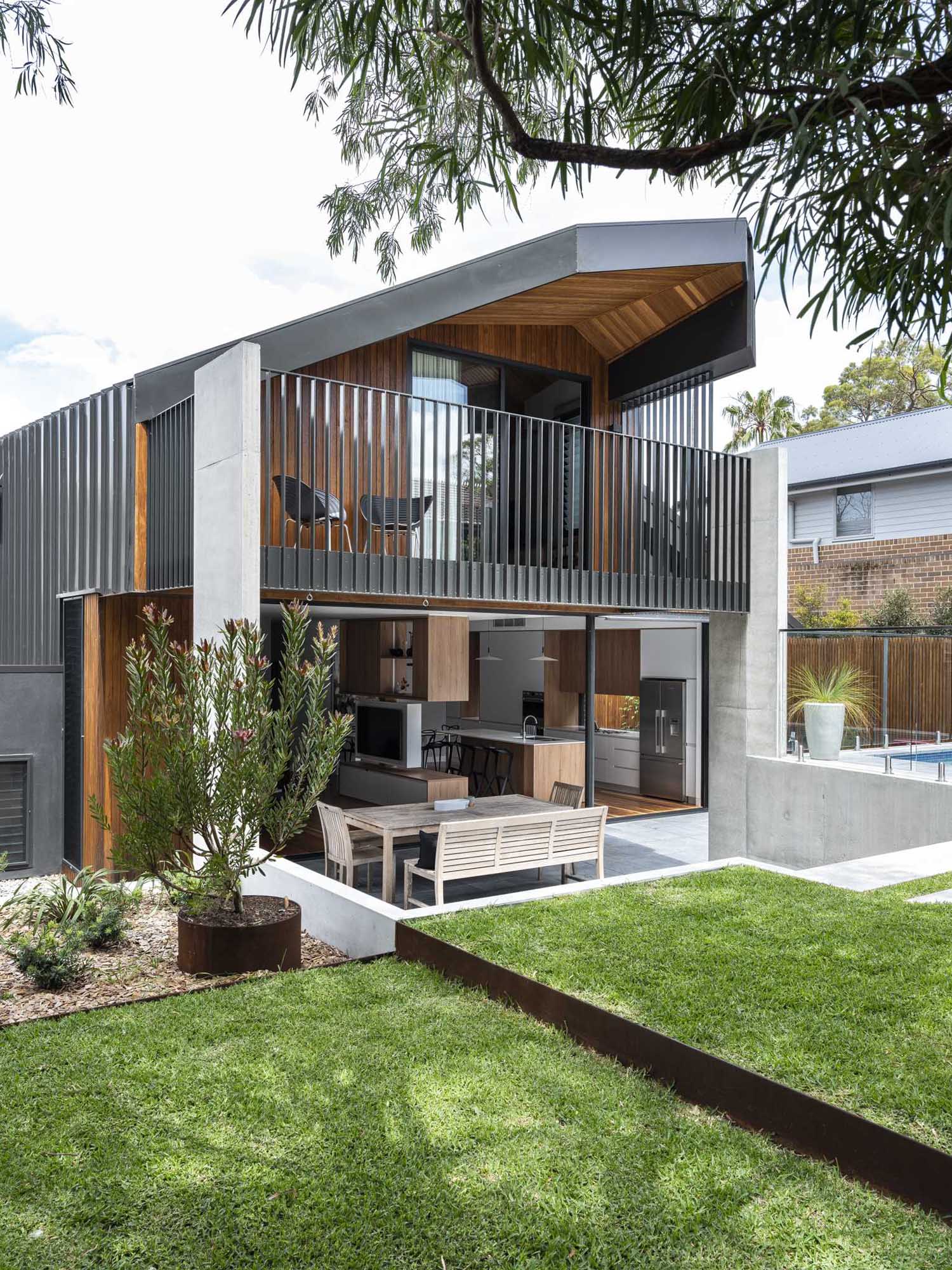 Steps lead from the yard down to a covered outdoor area, furnished for outdoor dining in the shade.