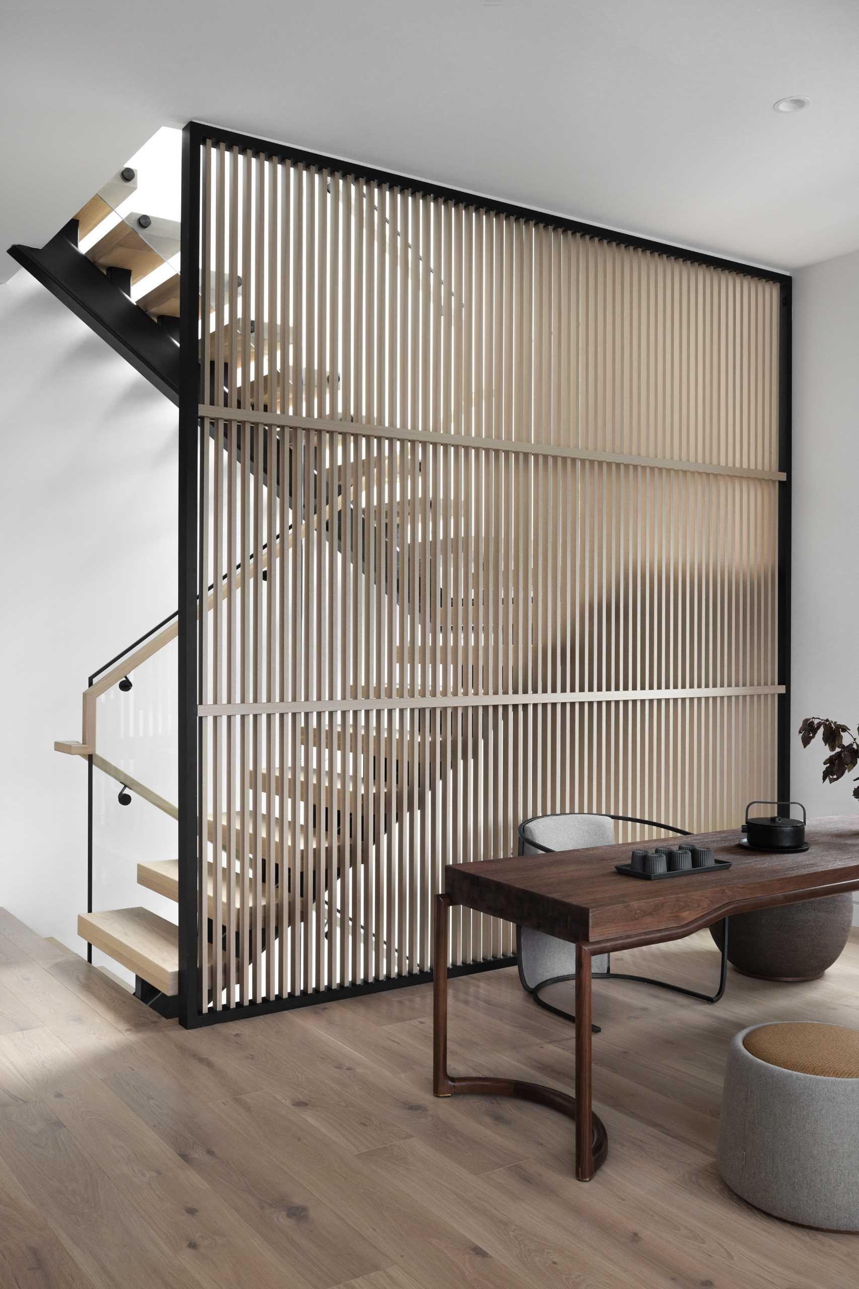 Wood and metal stairs, alongside a wood partition, lead to the basement and the upper level of this modern home.