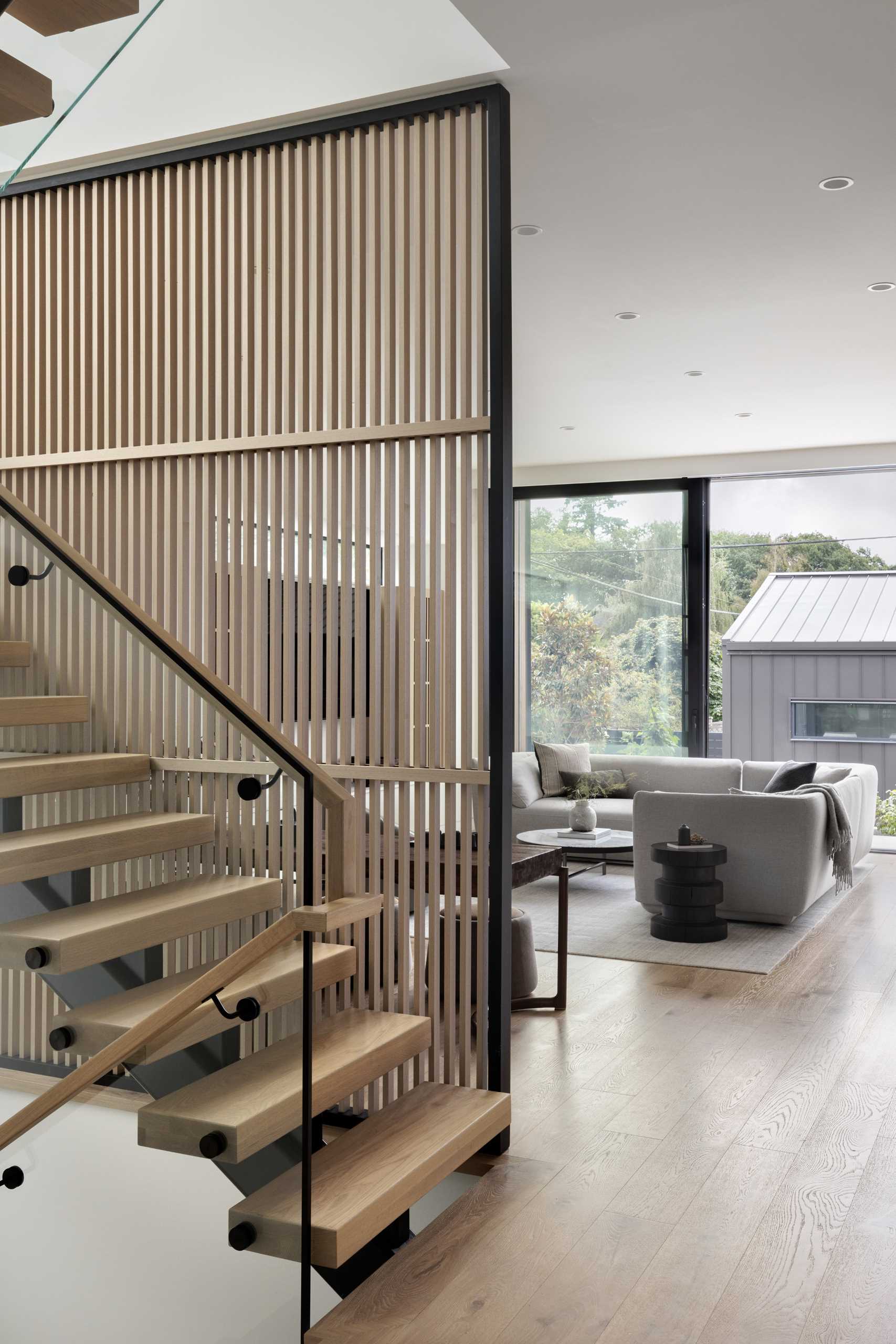 Wood and metal stairs, alongside a wood partition, lead to the basement and the upper level of this modern home.