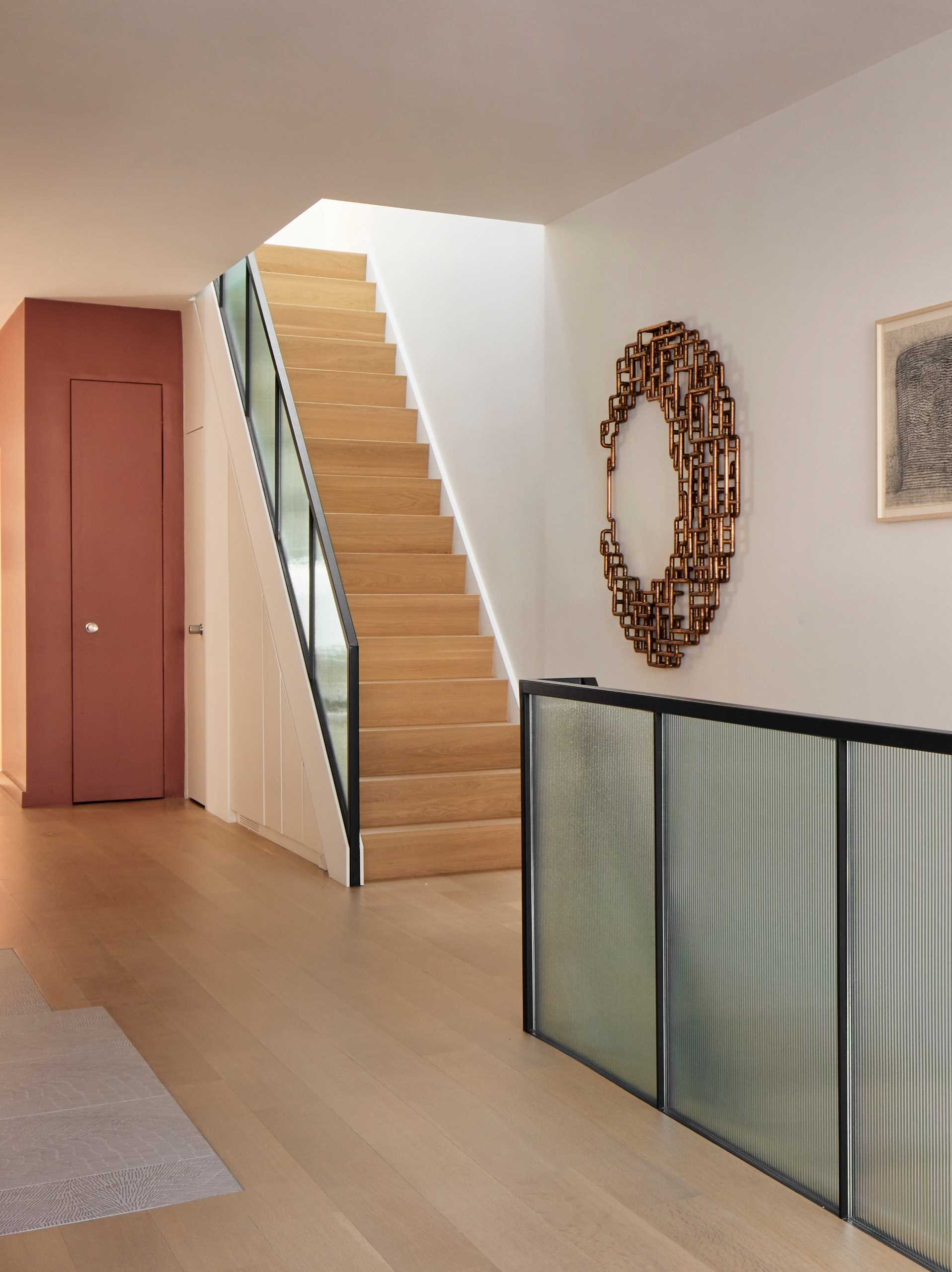 A wood staircase with a reeded glass and steel stair rail .