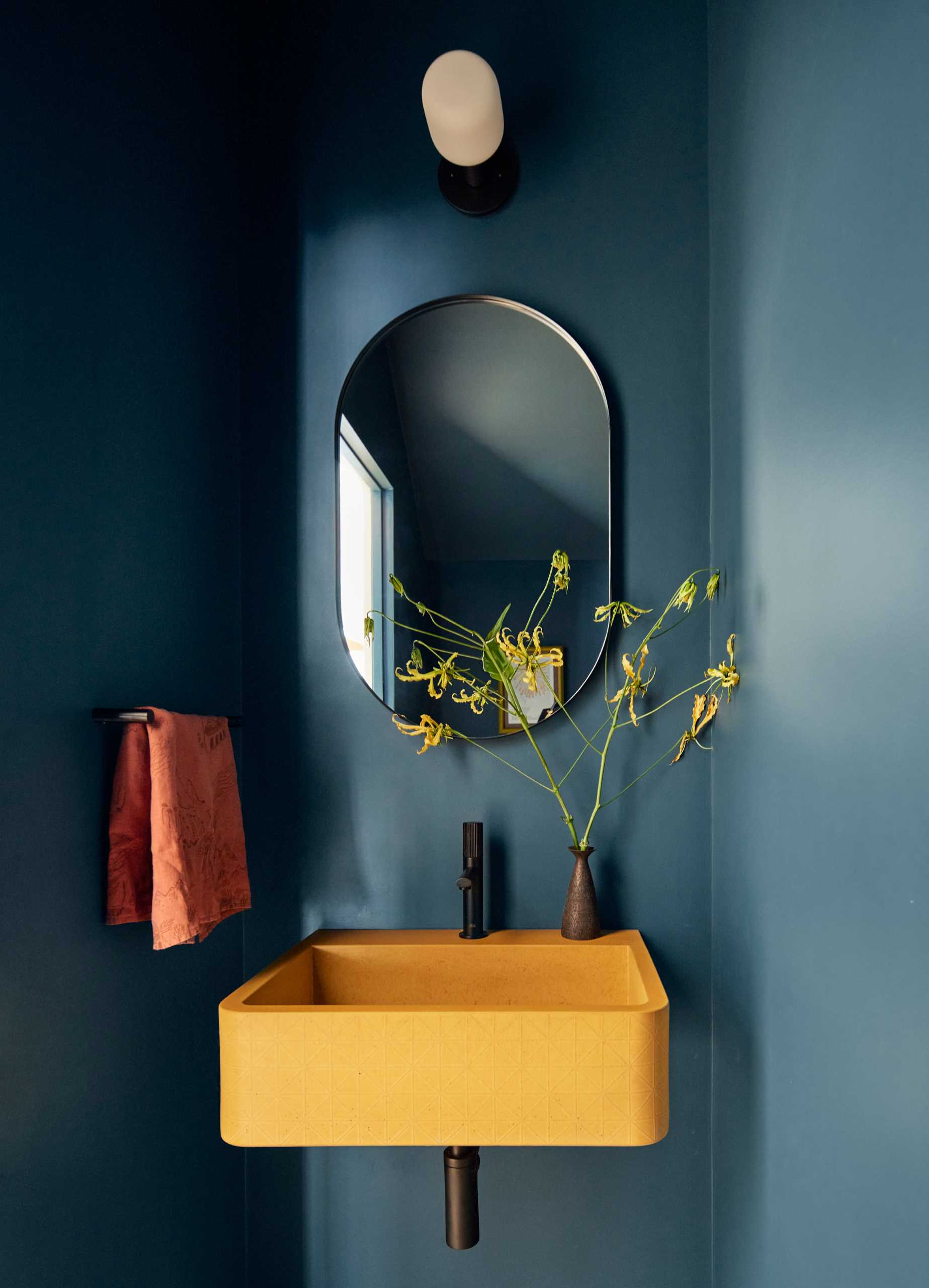 A modern powder room painted in a deep blue-black with a pop of yellow provided by a Kast concrete sink.